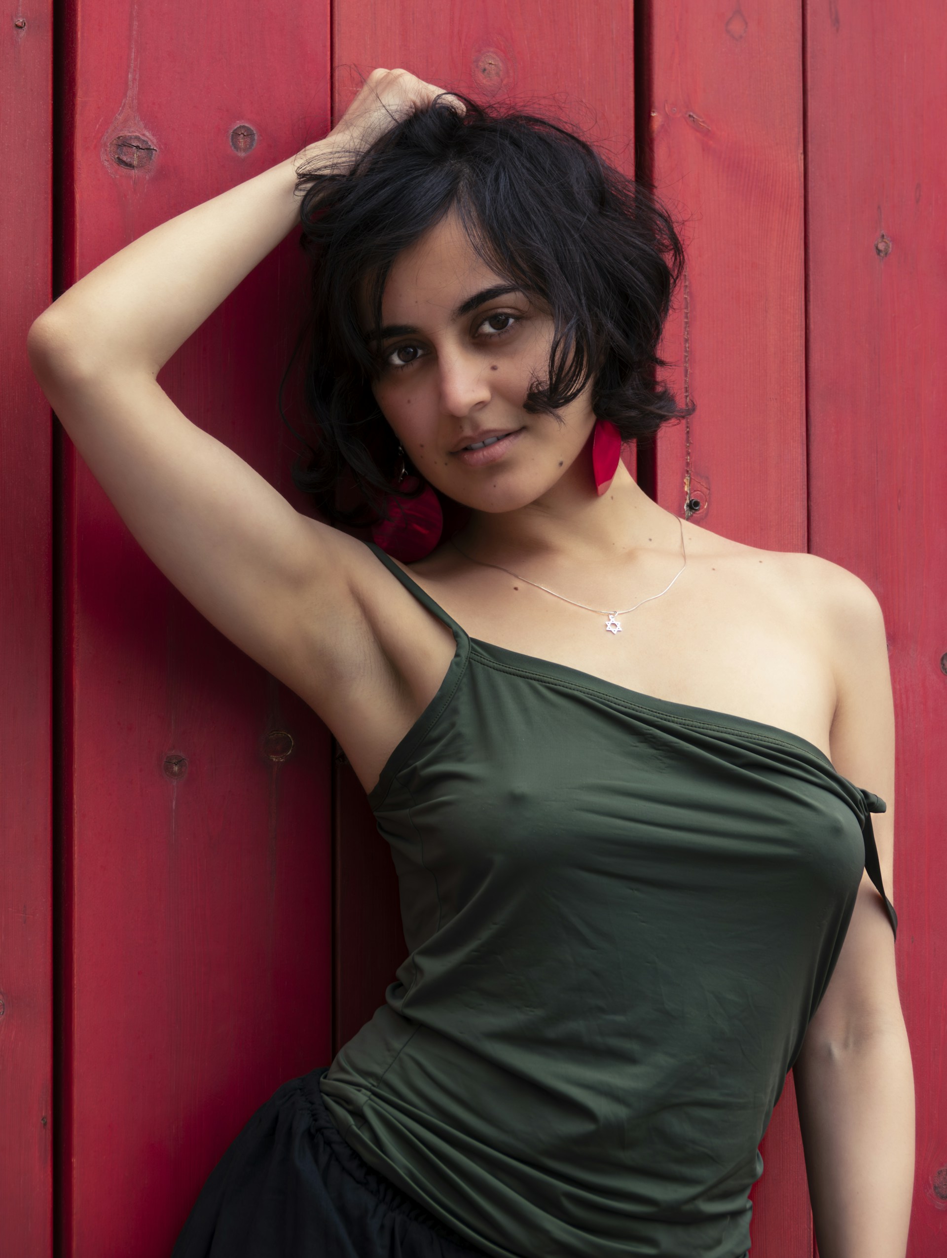A woman leaning against a red wall with her hand on her head