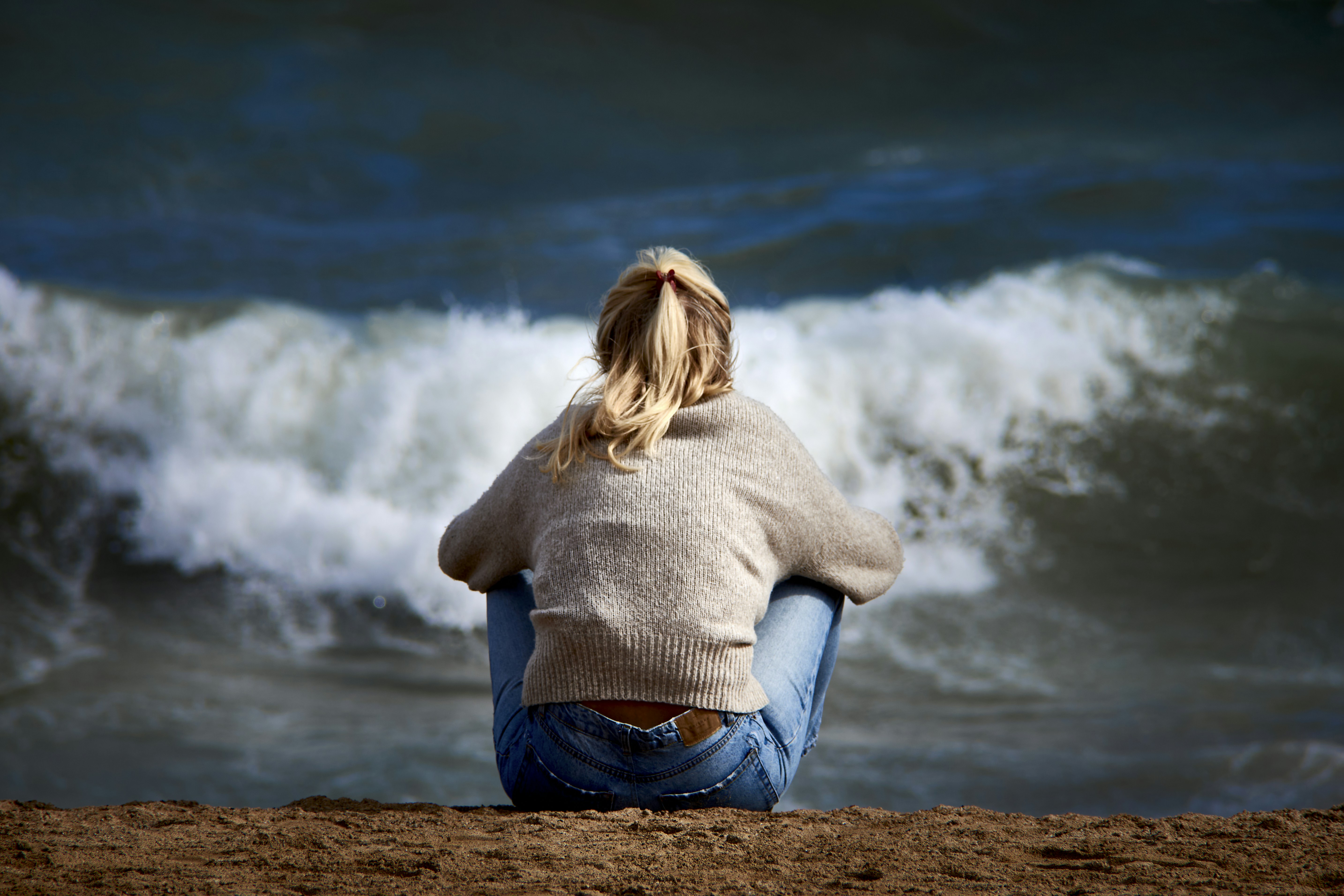 A woman sitting on a beach next to a body of water