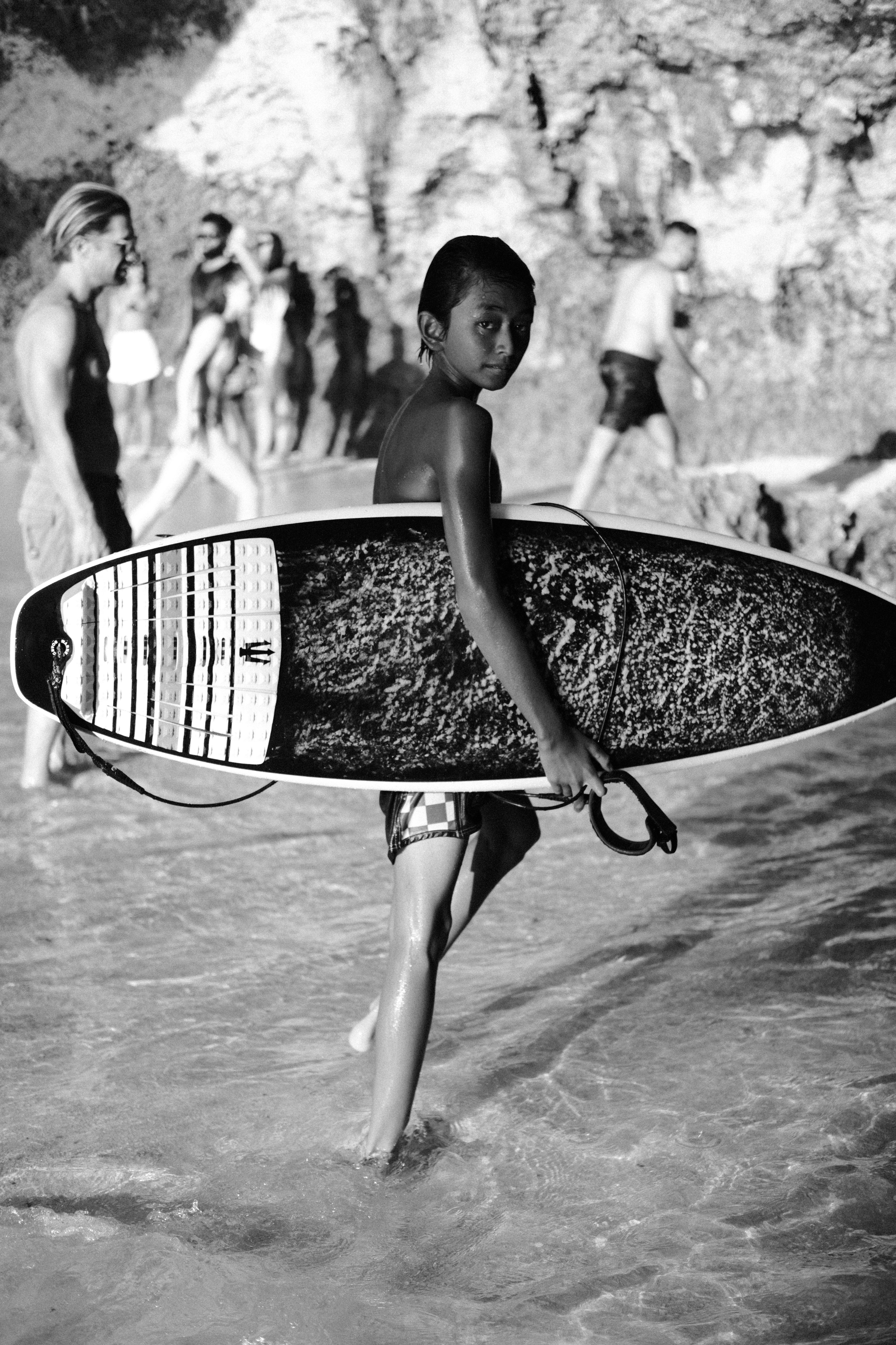 A young boy carrying a surfboard into the ocean