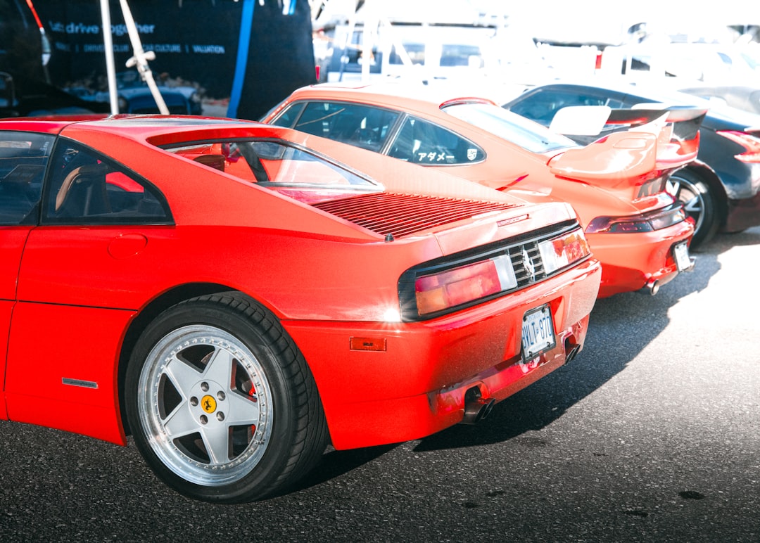 A red sports car parked in a parking lot, This image shows a group of exotic cars parked together, with a red Ferrari in the foreground and a Porsche in the background. The composition brings out the diversity in design between these high-end cars, capturing the essence of a car meet. The cars’ vibrant colors pop against the neutral asphalt background.