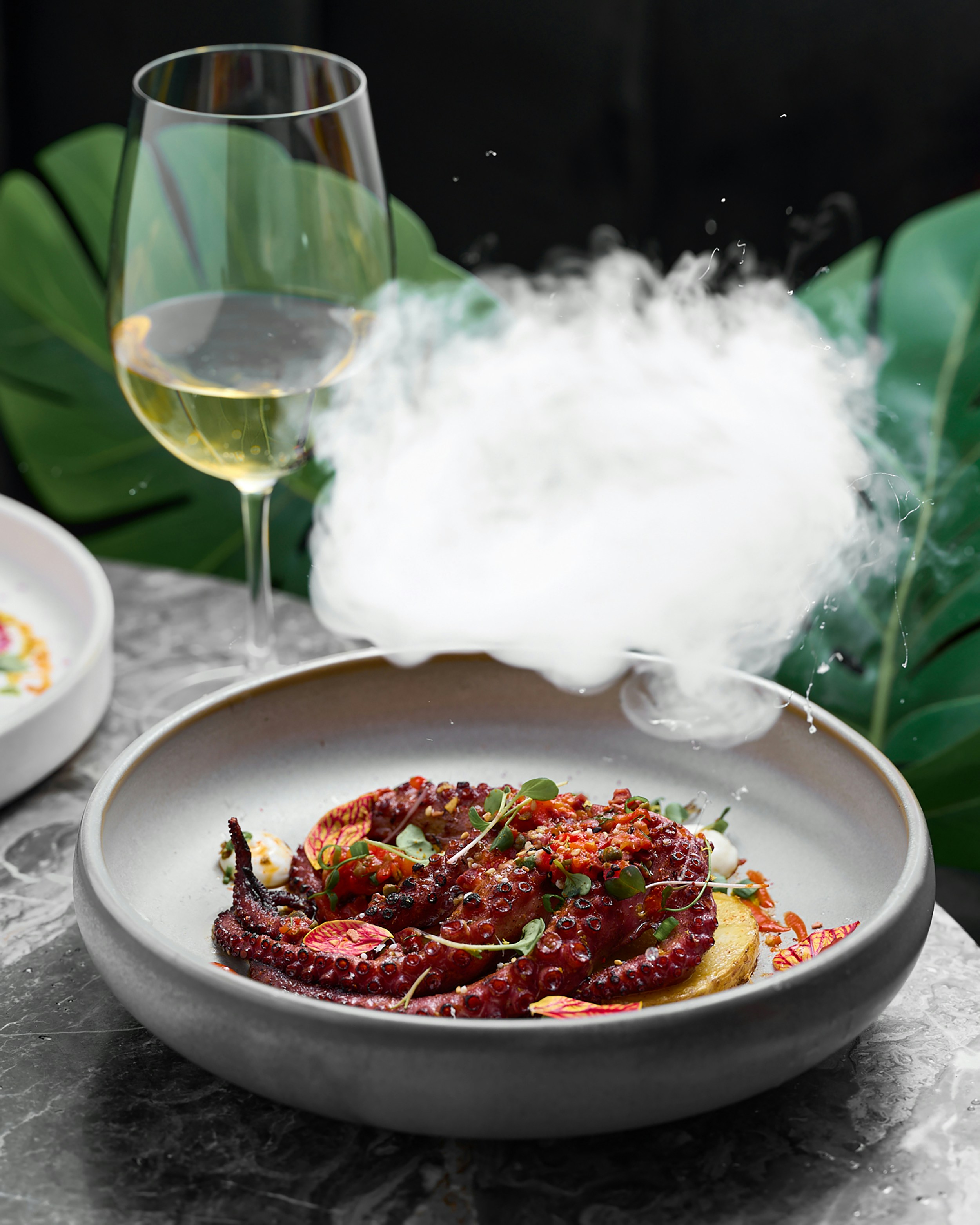 A white plate topped with food next to a glass of wine