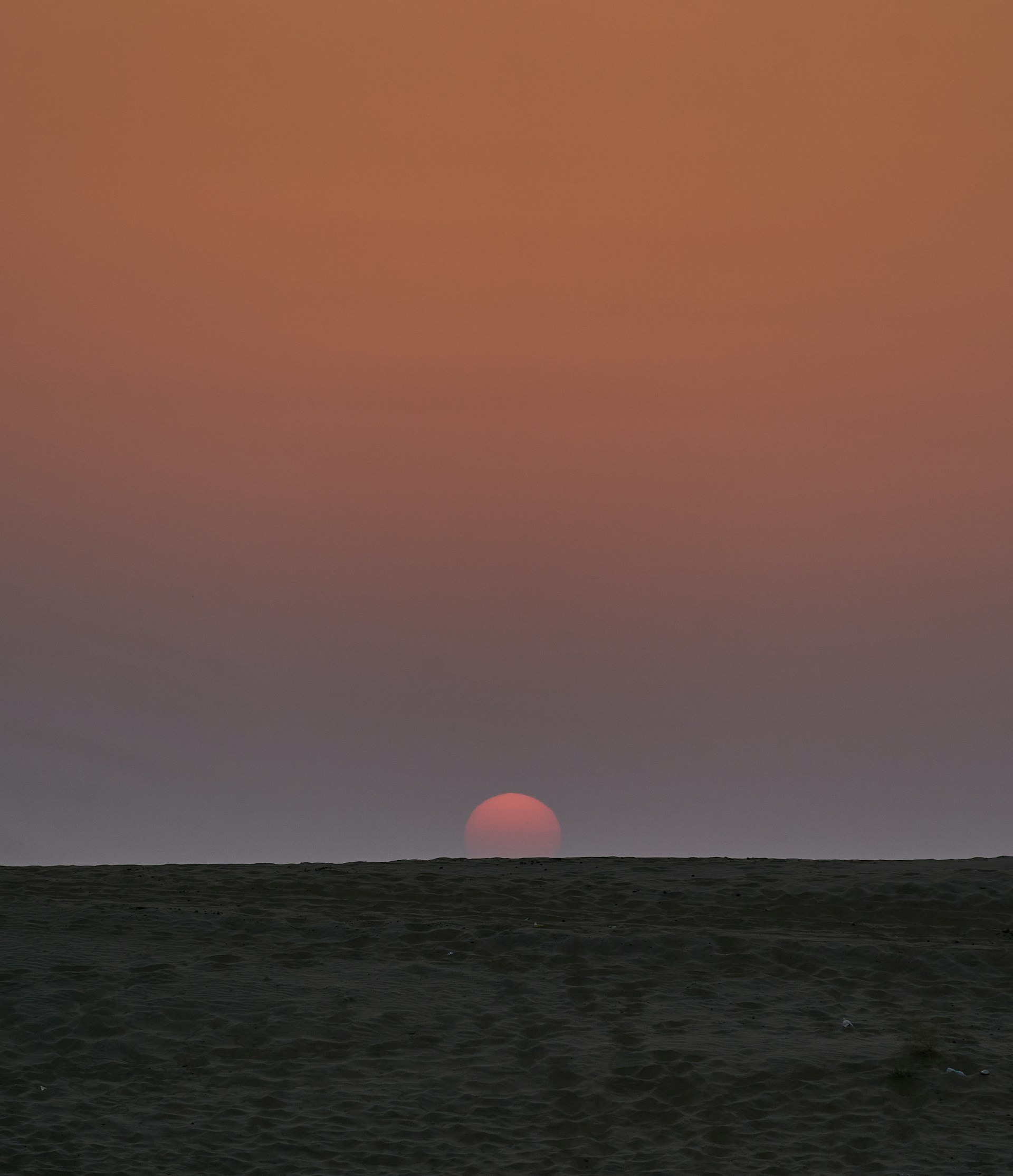 The sun is setting over the horizon of the desert