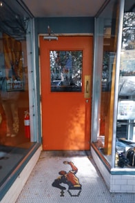 A store front with an orange door and a black and white tiled floor