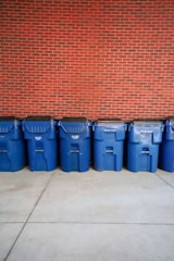 A row of blue trash cans sitting in front of a brick wall