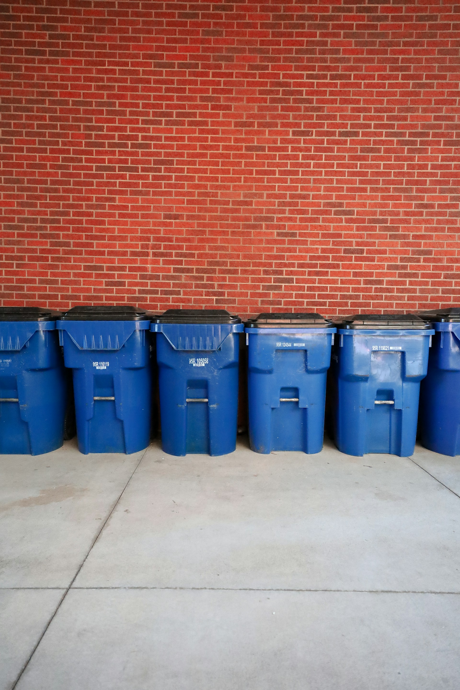 A row of blue trash cans sitting in front of a brick wall