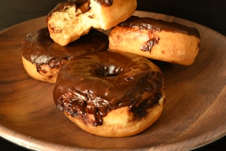 A wooden plate topped with chocolate covered donuts