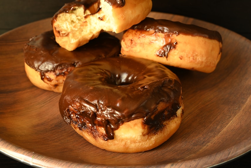 A wooden plate topped with chocolate covered donuts