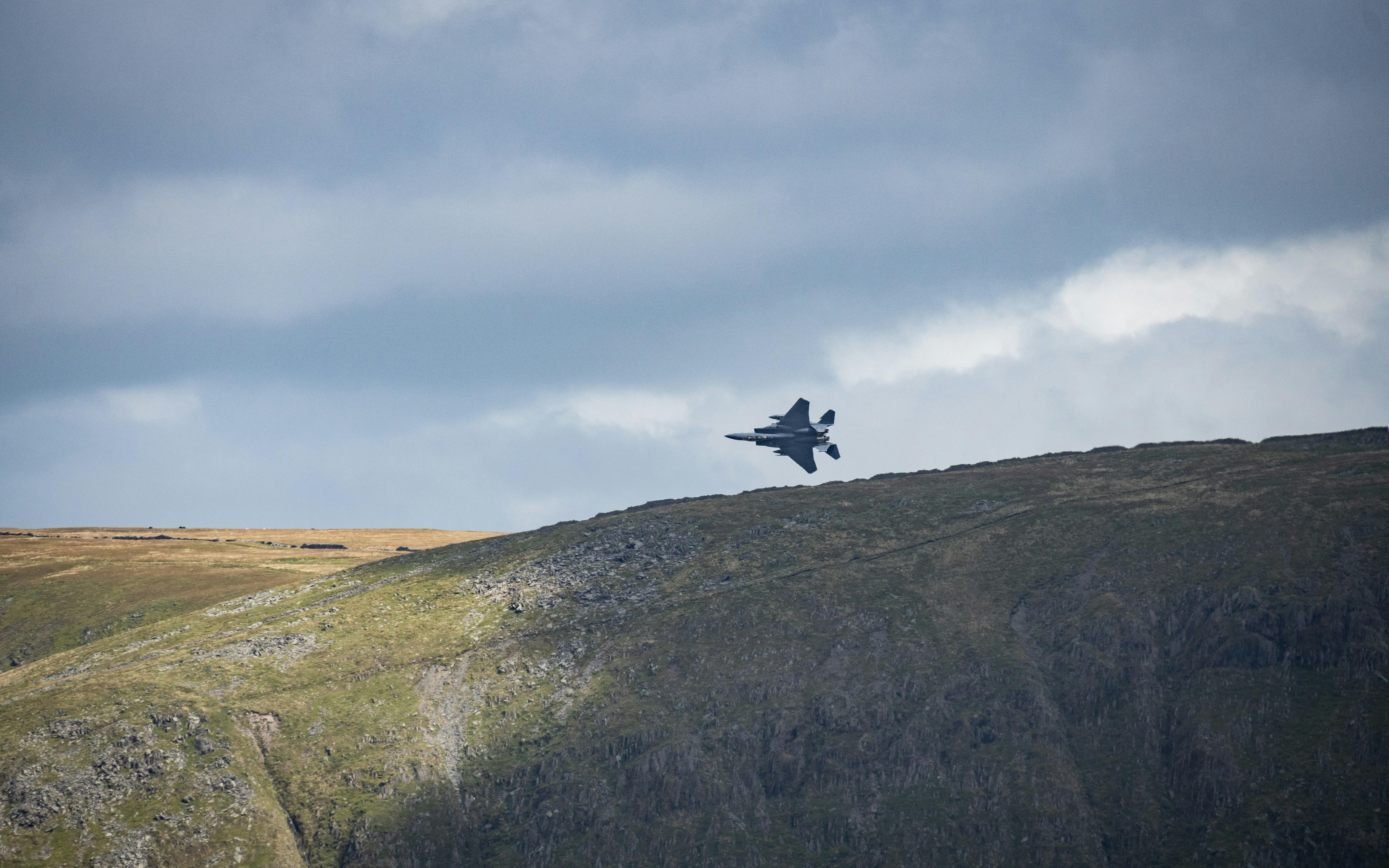 A fighter jet flying over a lush green hillside