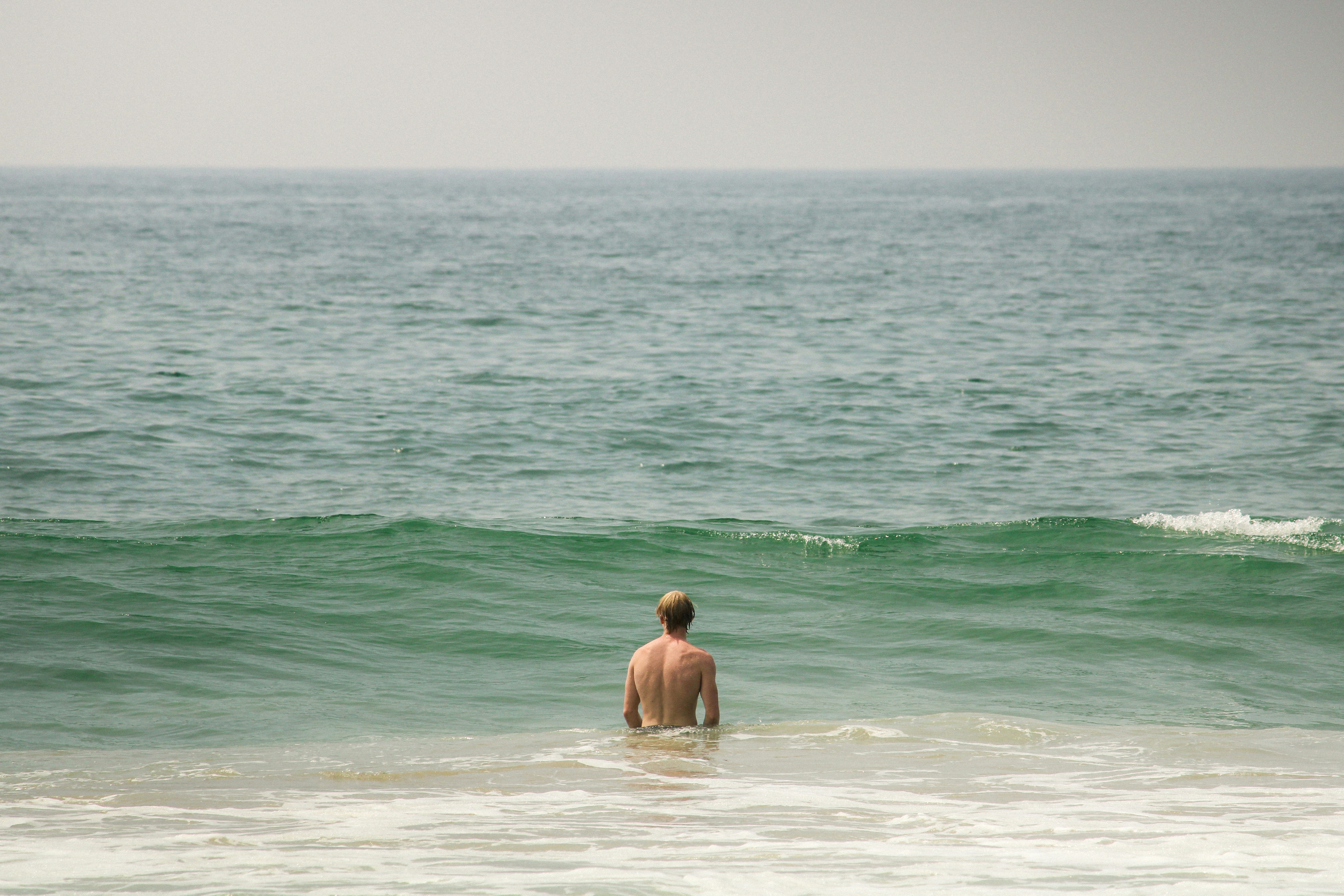 A man standing in the ocean with his back to the camera