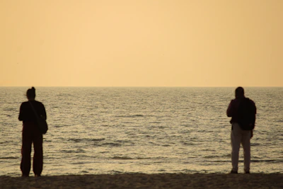 Two people standing on a beach watching the ocean