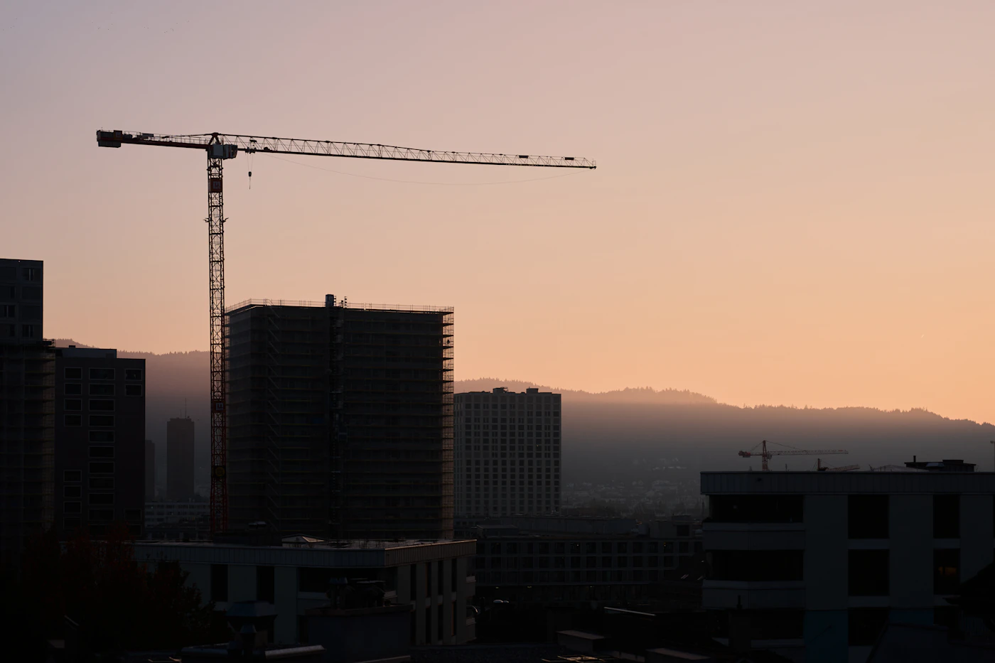 Construction crane at dusk over a high-rise under construction