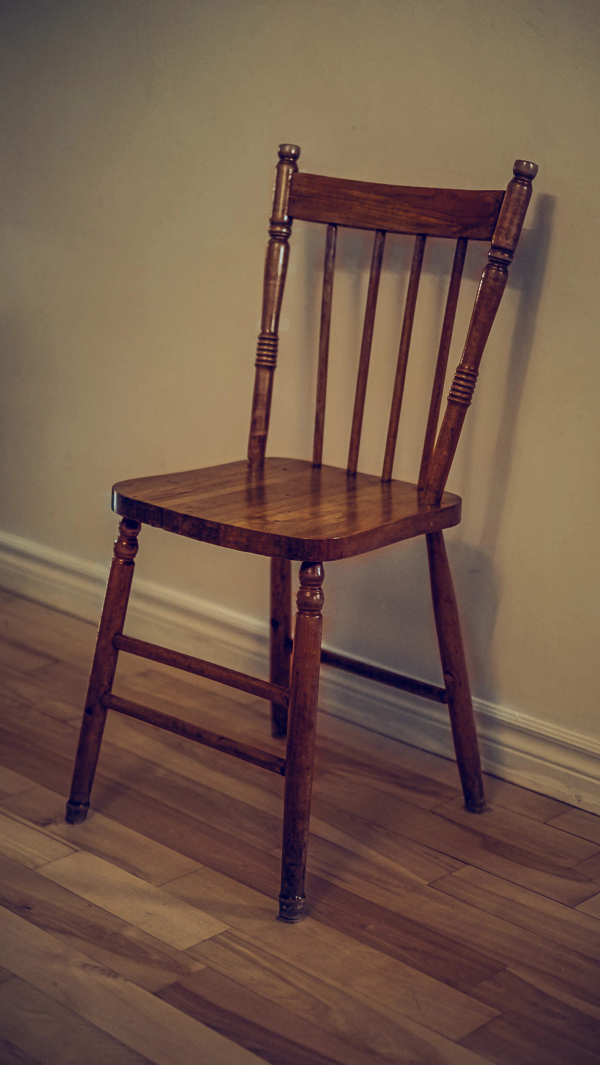 A simple wooden chair on a wooden floor against a pale wall