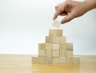 A hand is placing a piece of wood into a pyramid