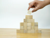 A hand is placing a piece of wood into a pyramid