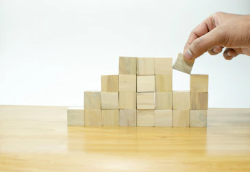 A person placing a block into a pile of wooden blocks