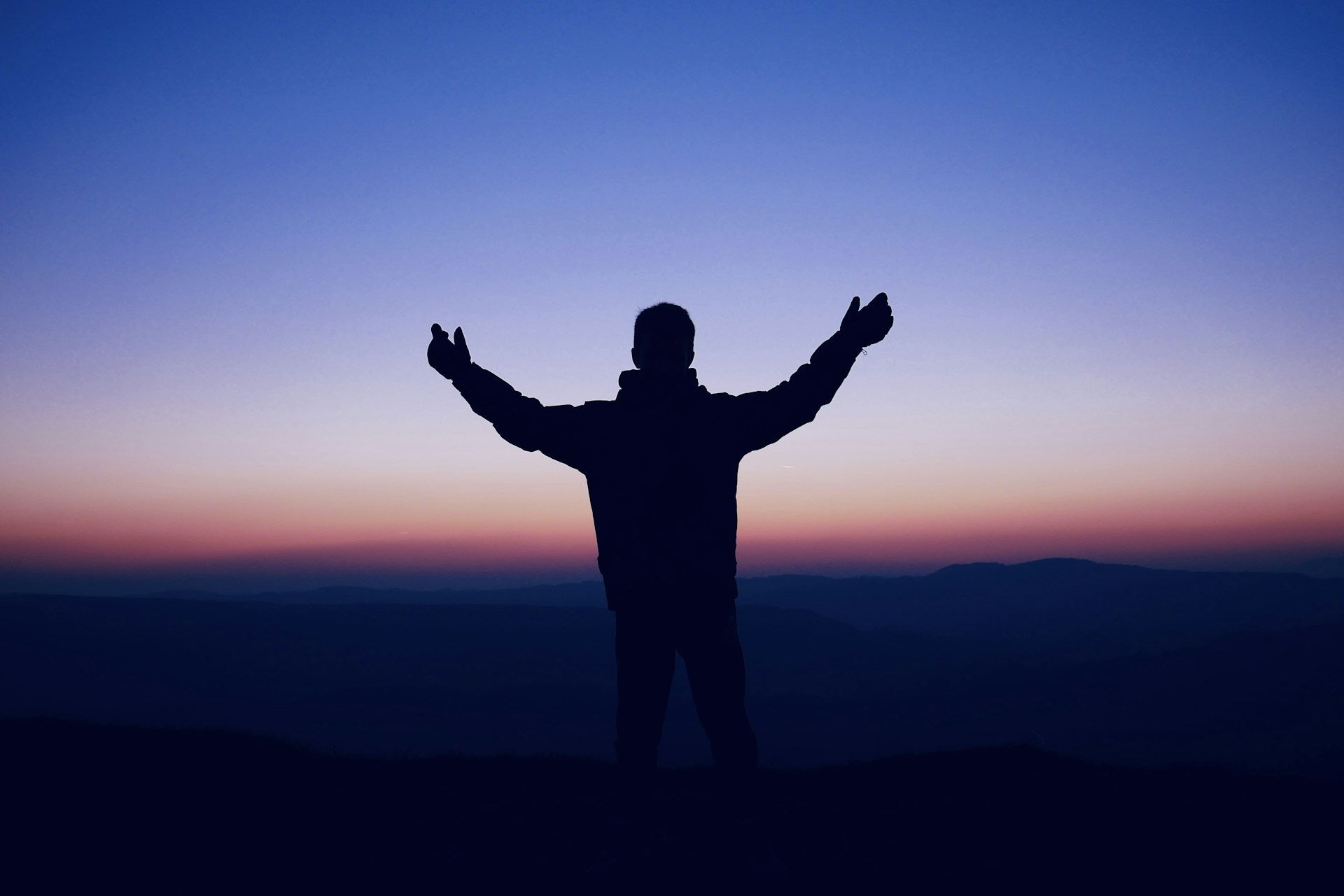 A man standing on top of a hill with his arms outstretched