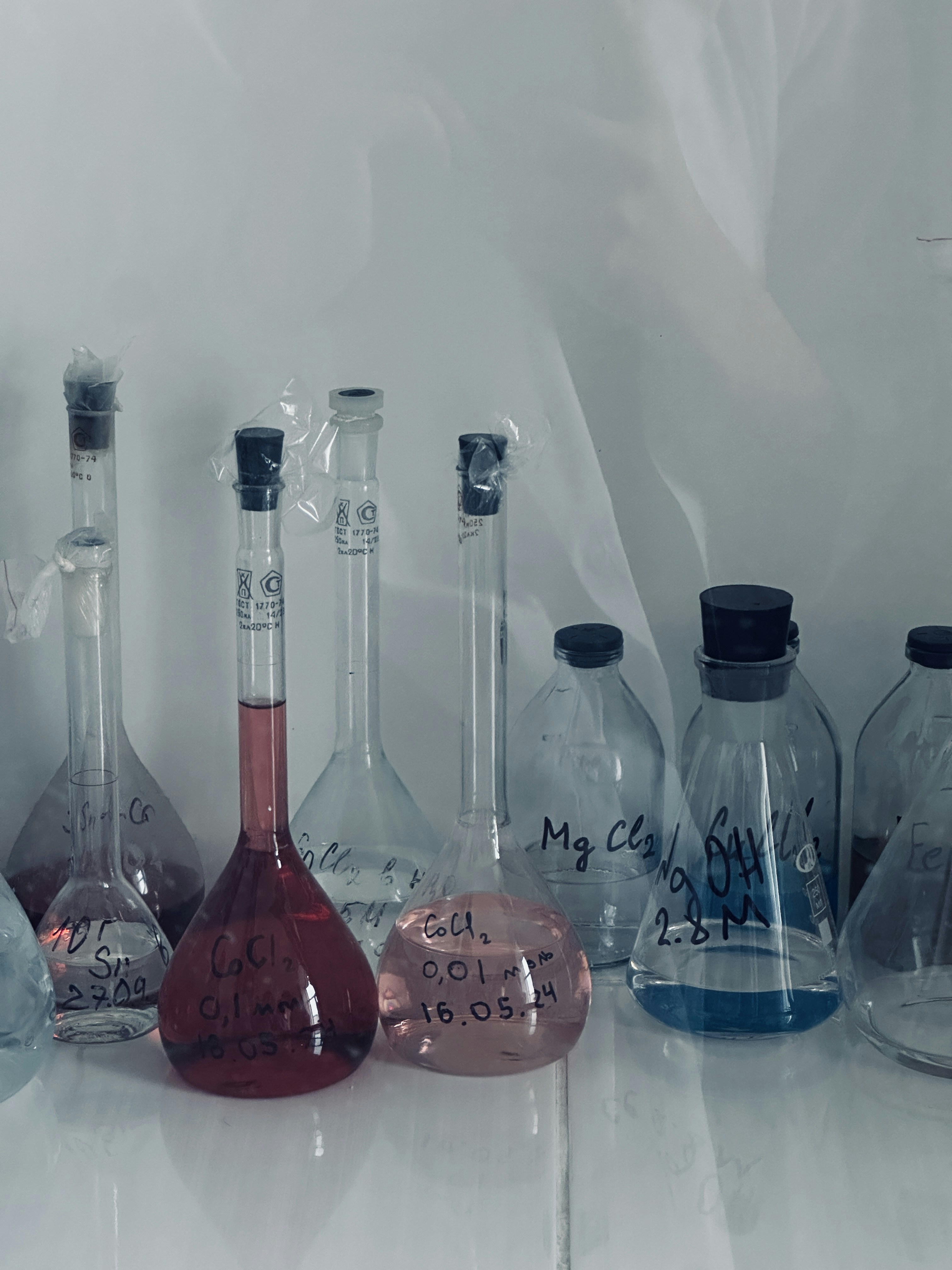 Chemistry lab with bright overhead lighting, colorful liquids in flasks, clean white benches