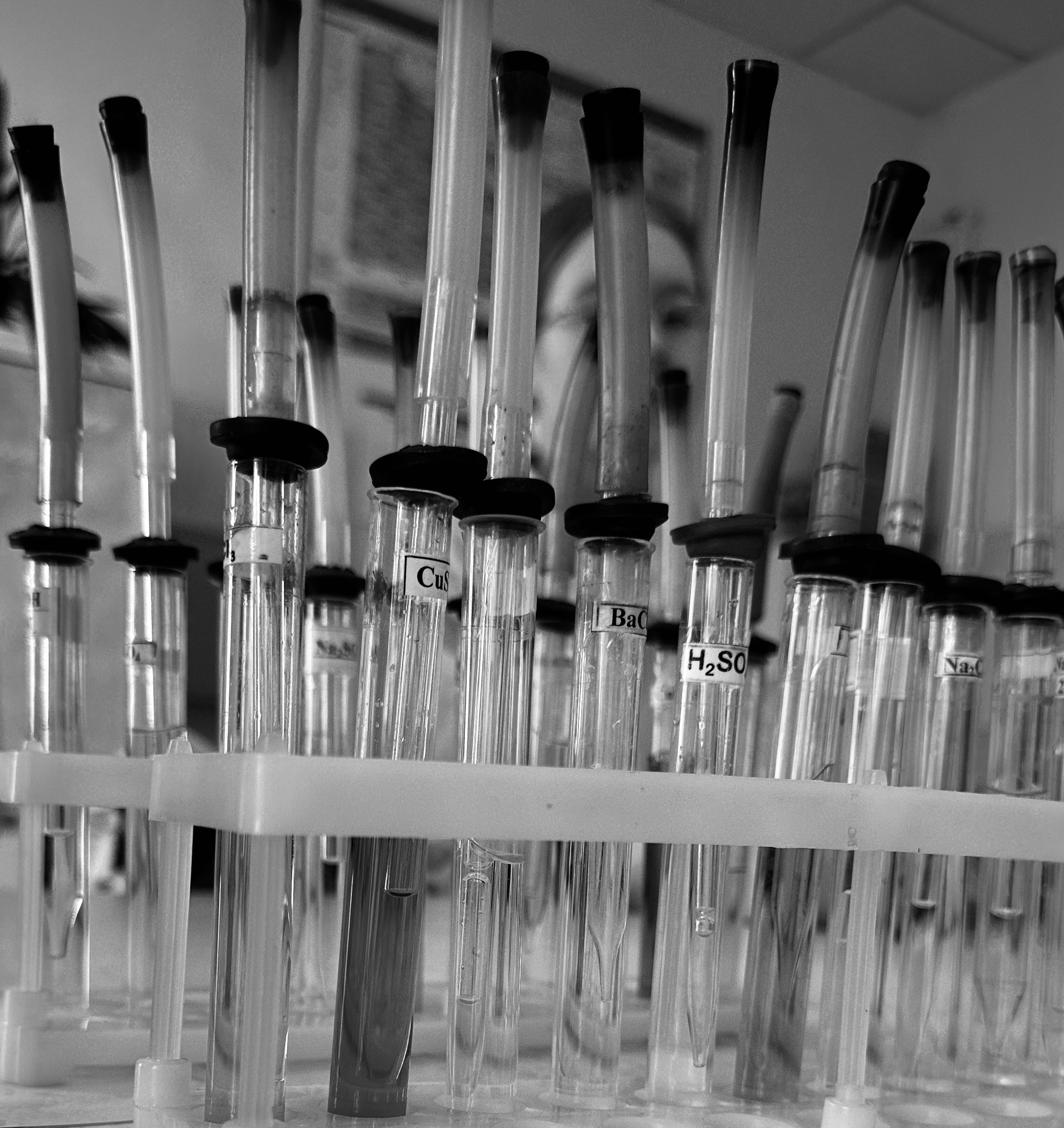 Clear glass test tubes arranged in rack on bright white laboratory bench with scientific equipment