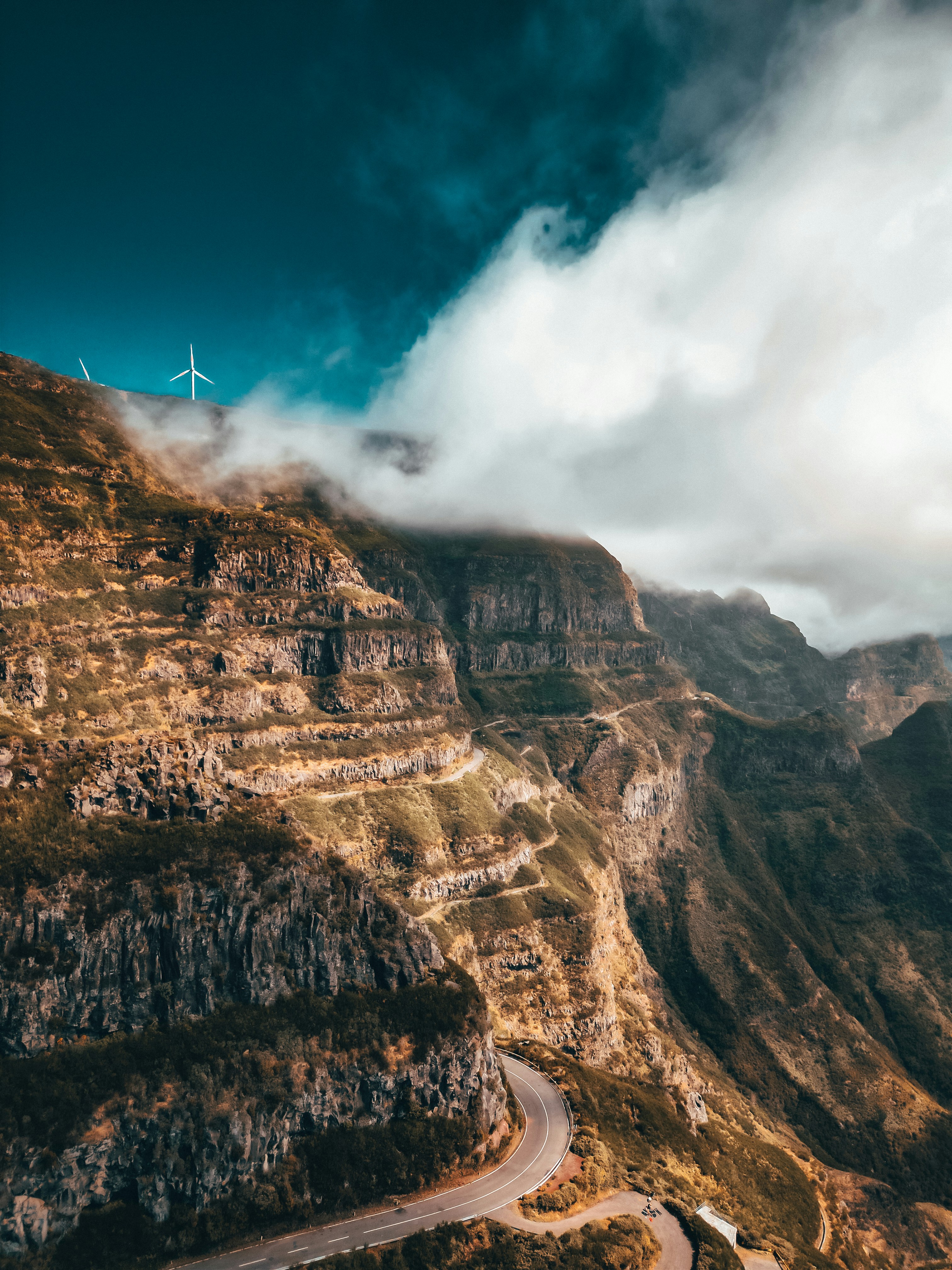 A winding mountain road with a wind turbine in the distance