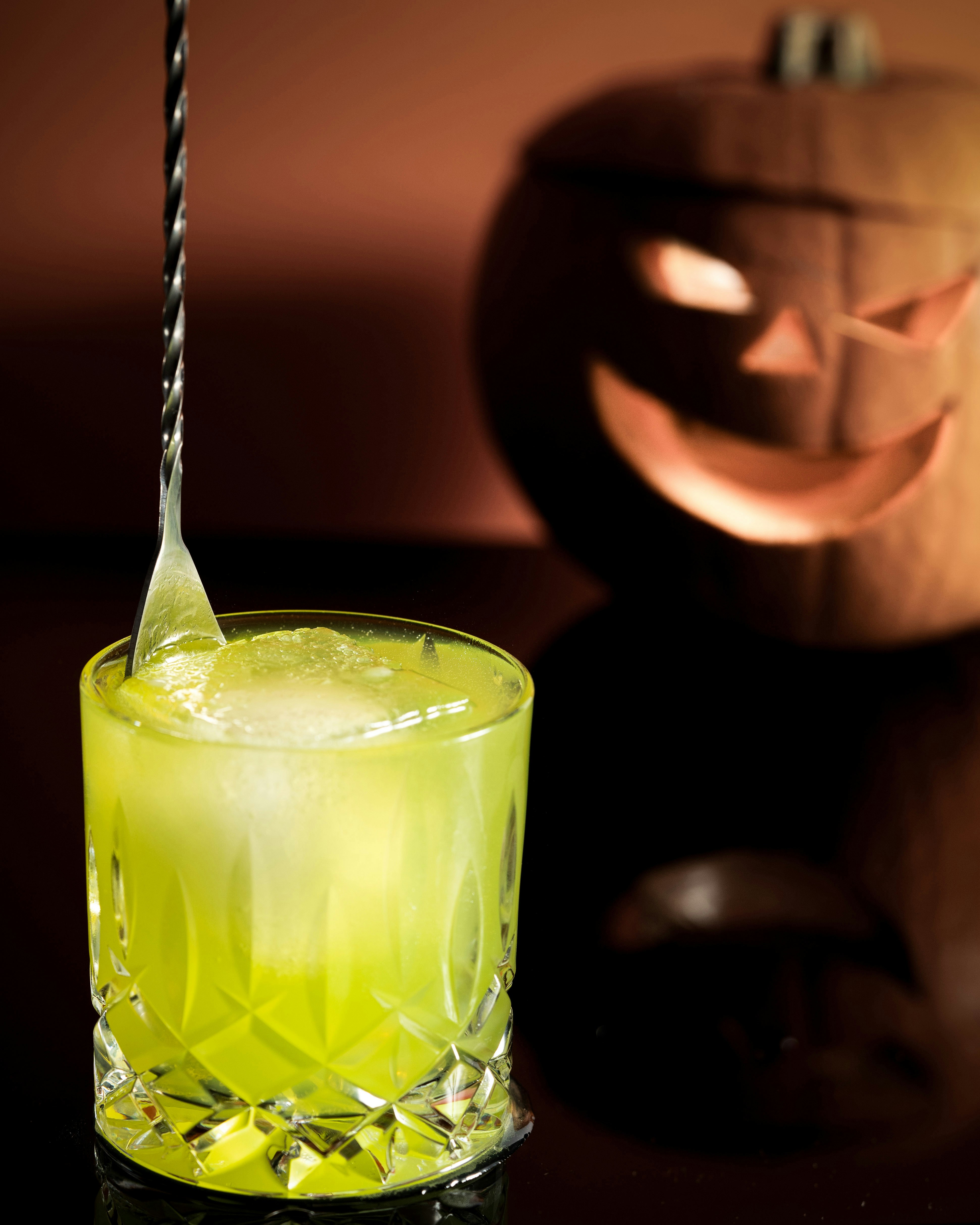 A green drink in a glass next to a carved pumpkin