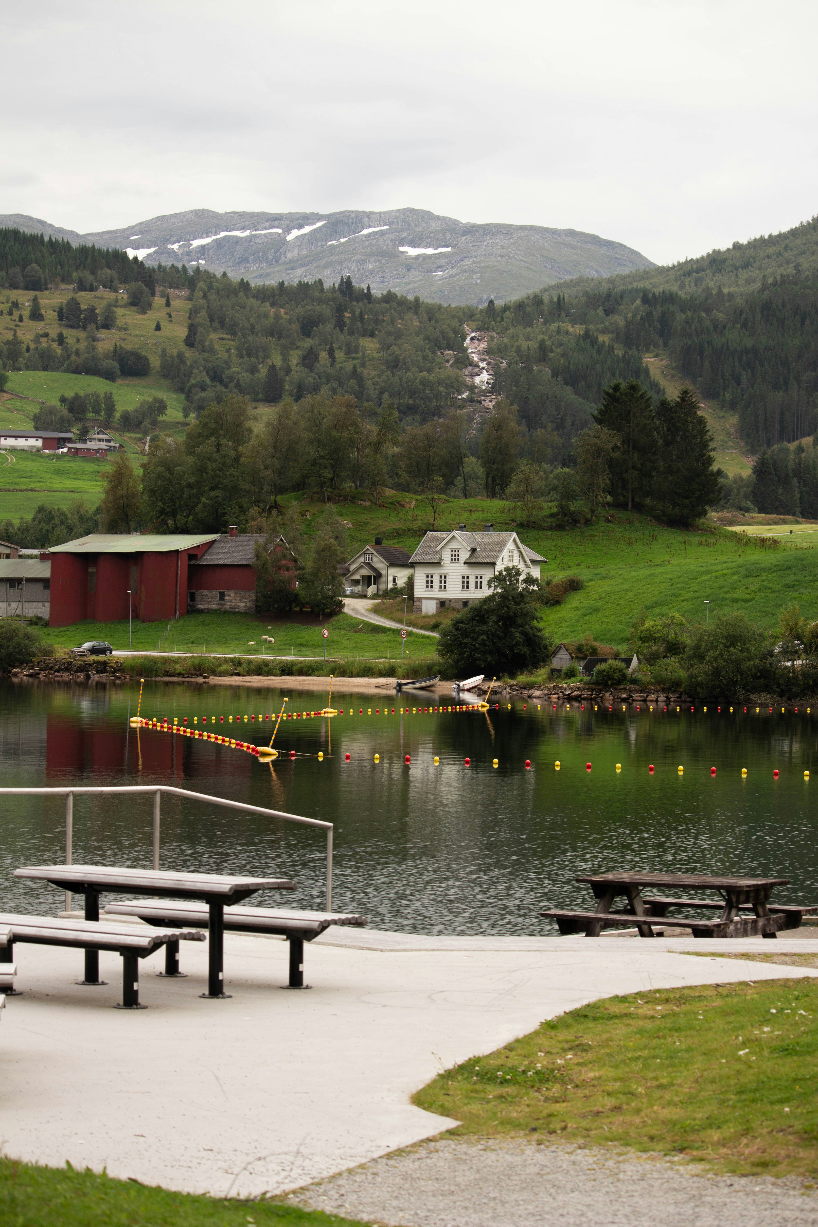 Træpicnicborde med udsigt over en sø med fjerntliggende farverige huse.