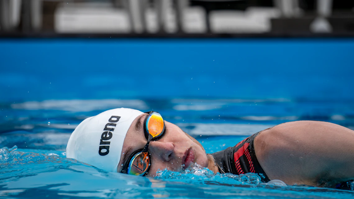 Swimmer wearing professional swim goggles and a swimming cap in a bright blue pool