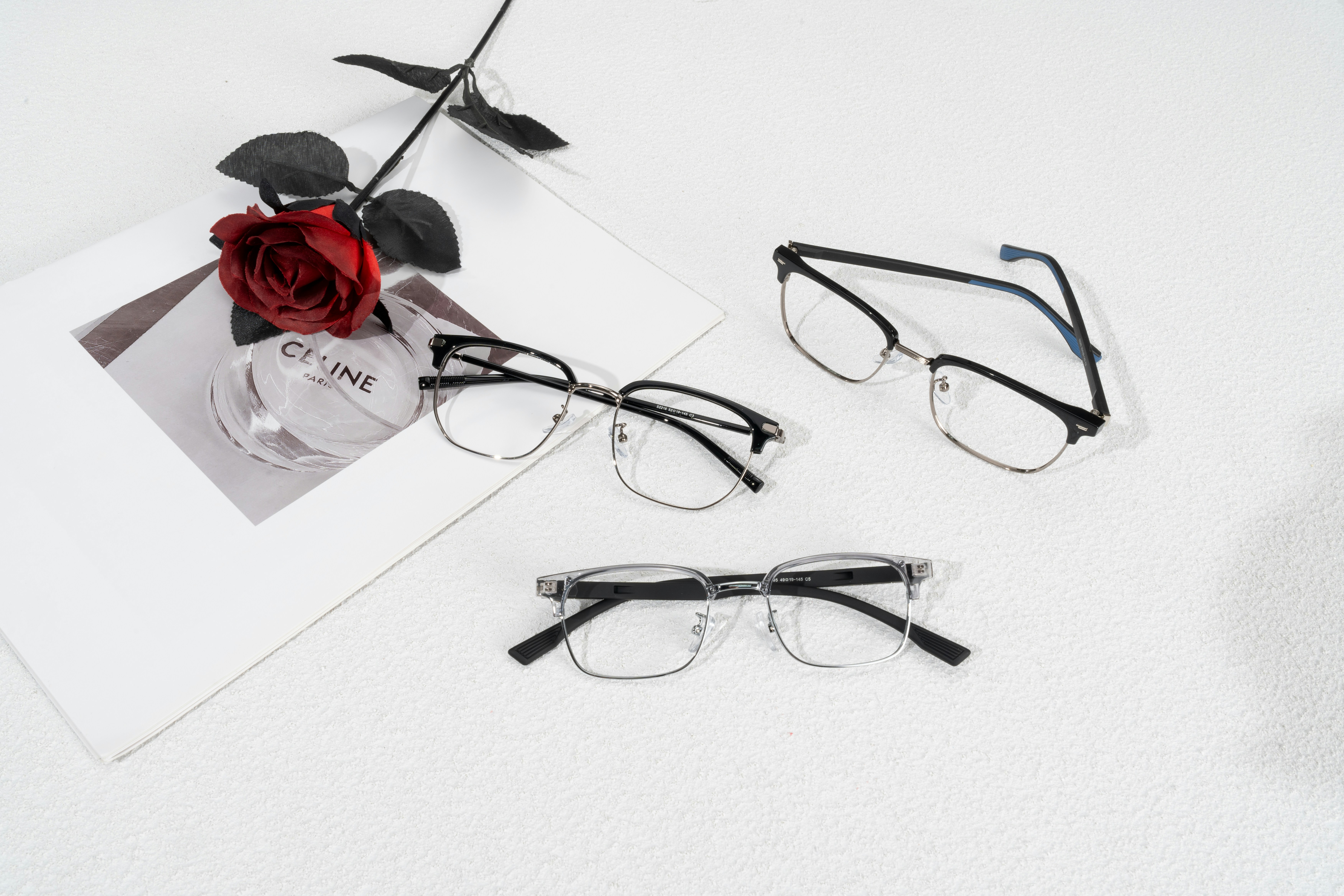 This chic collection of eyewear captures timeless elegance and versatility in three unique frame designs. With a soft red rose placed alongside, the scene exudes a touch of romance and refinement.