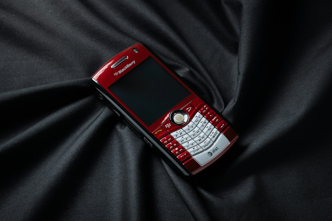 A red and white cell phone laying on a black cloth