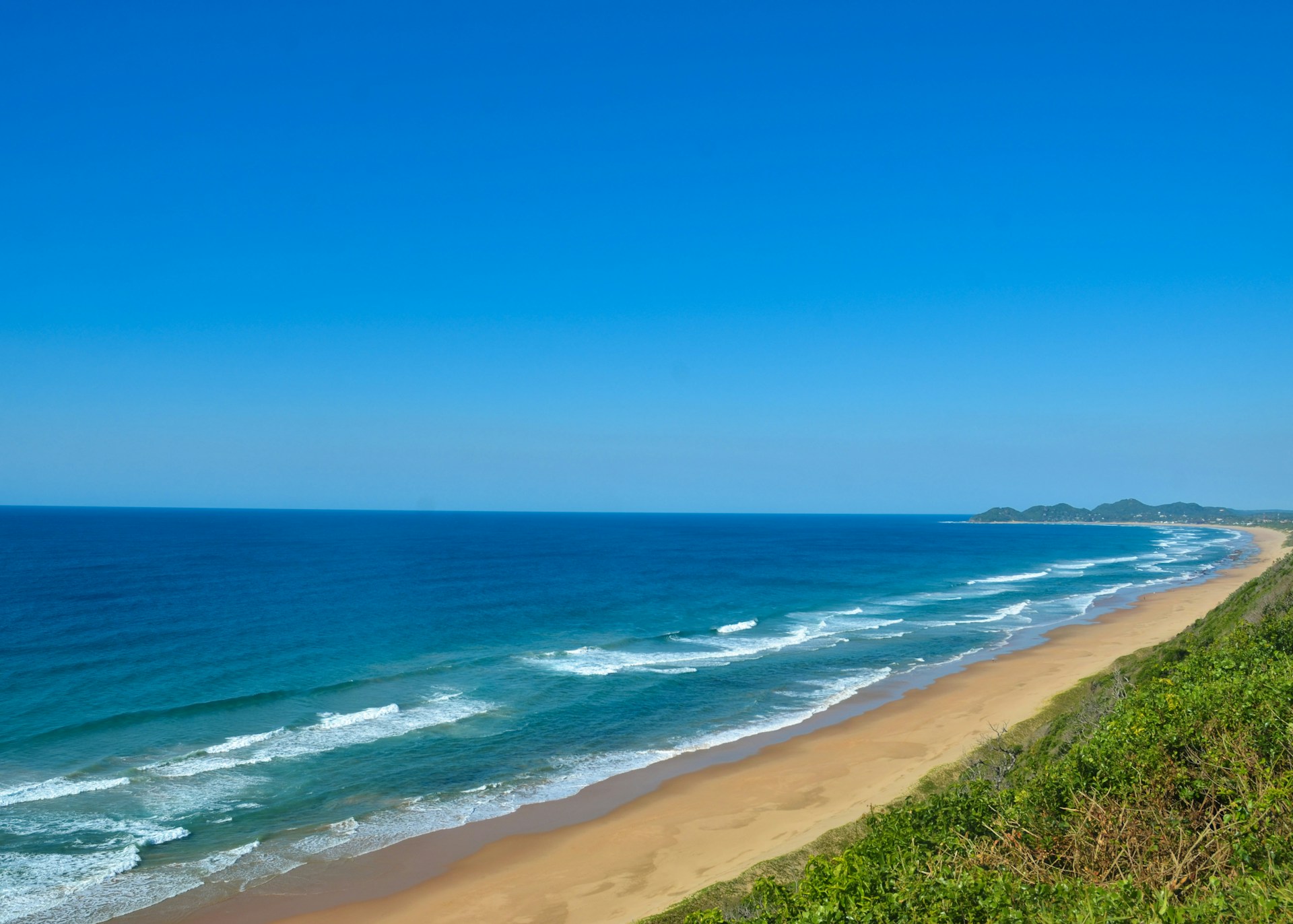A view of a beach from a hill overlooking the ocean