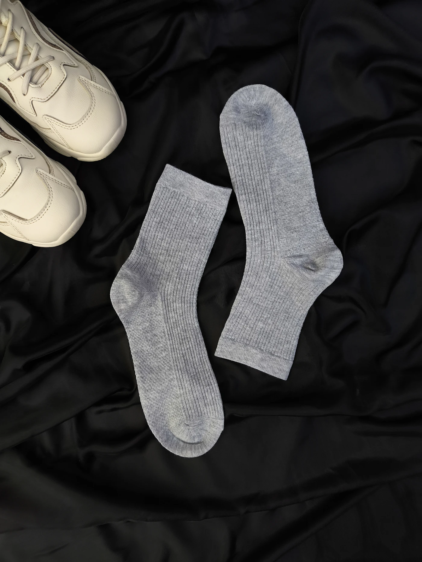 White sneakers and gray socks arranged on dark fabric