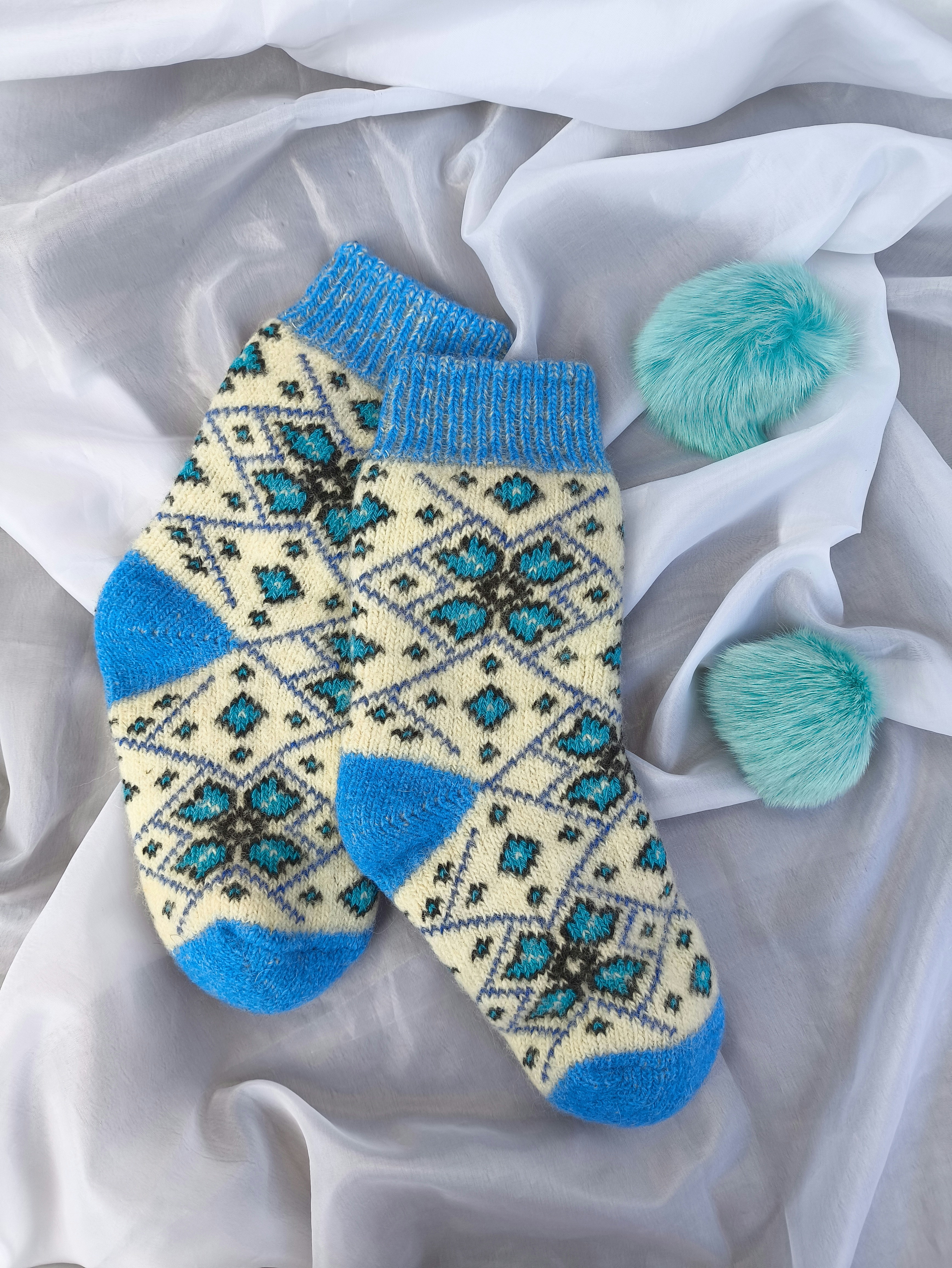 A pair of mittens and a pom pom on a white sheet