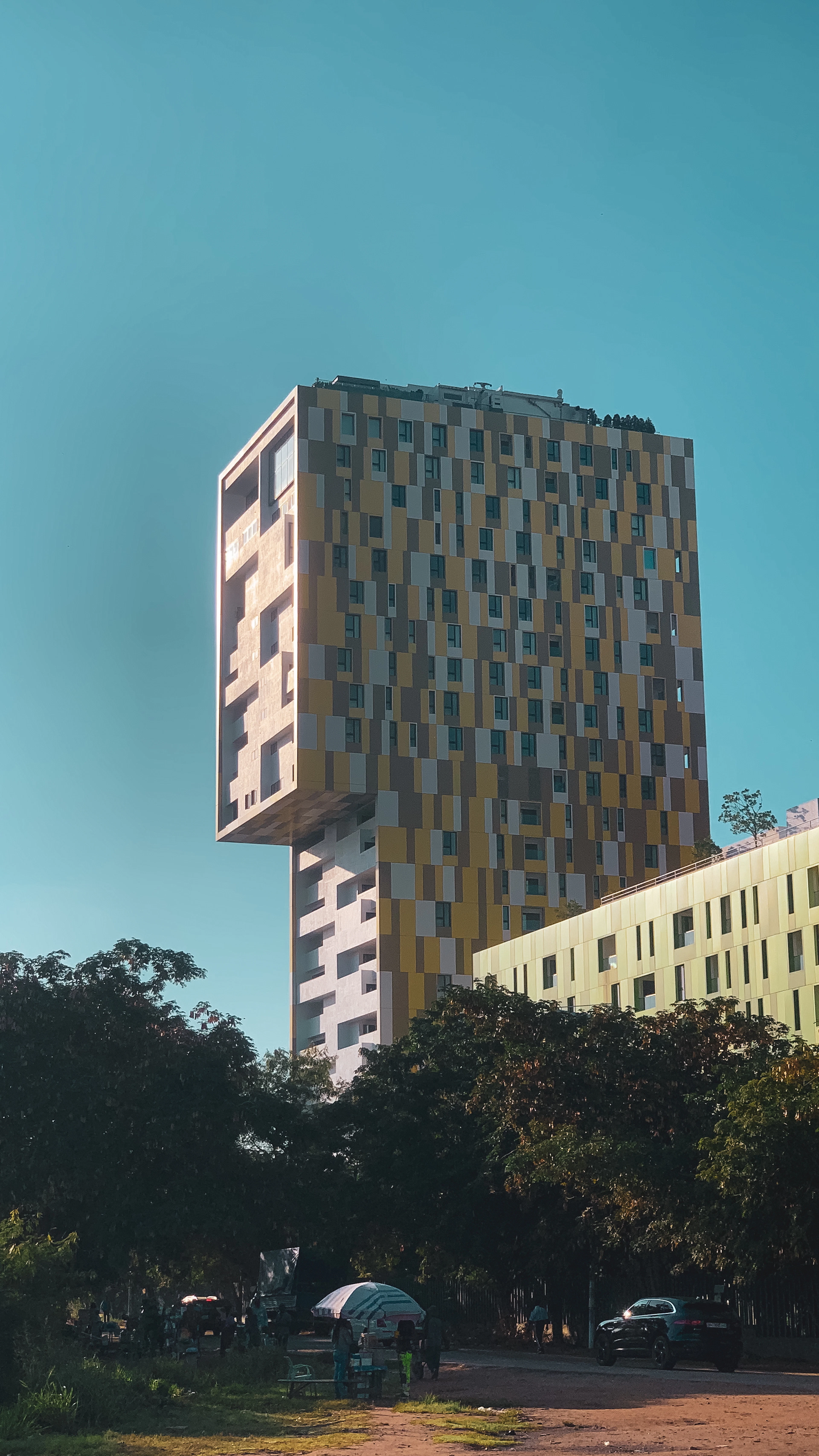 A striking cantilevered high-rise glows in late-afternoon light above a row of green trees.