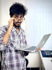 A man with glasses holding a laptop computer