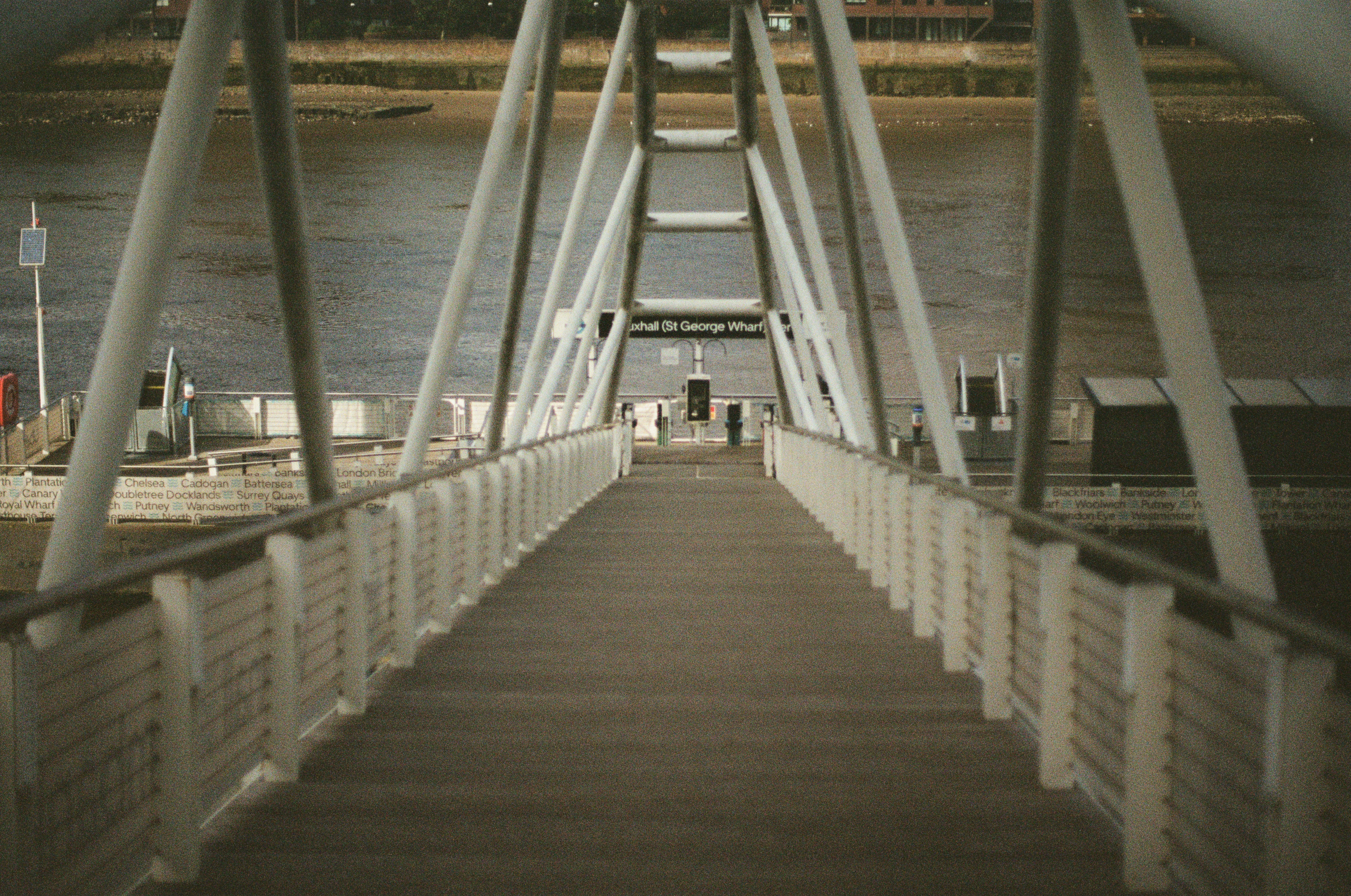 A modern pedestrian bridge with white railings and a wooden walkway spans over a calm river.