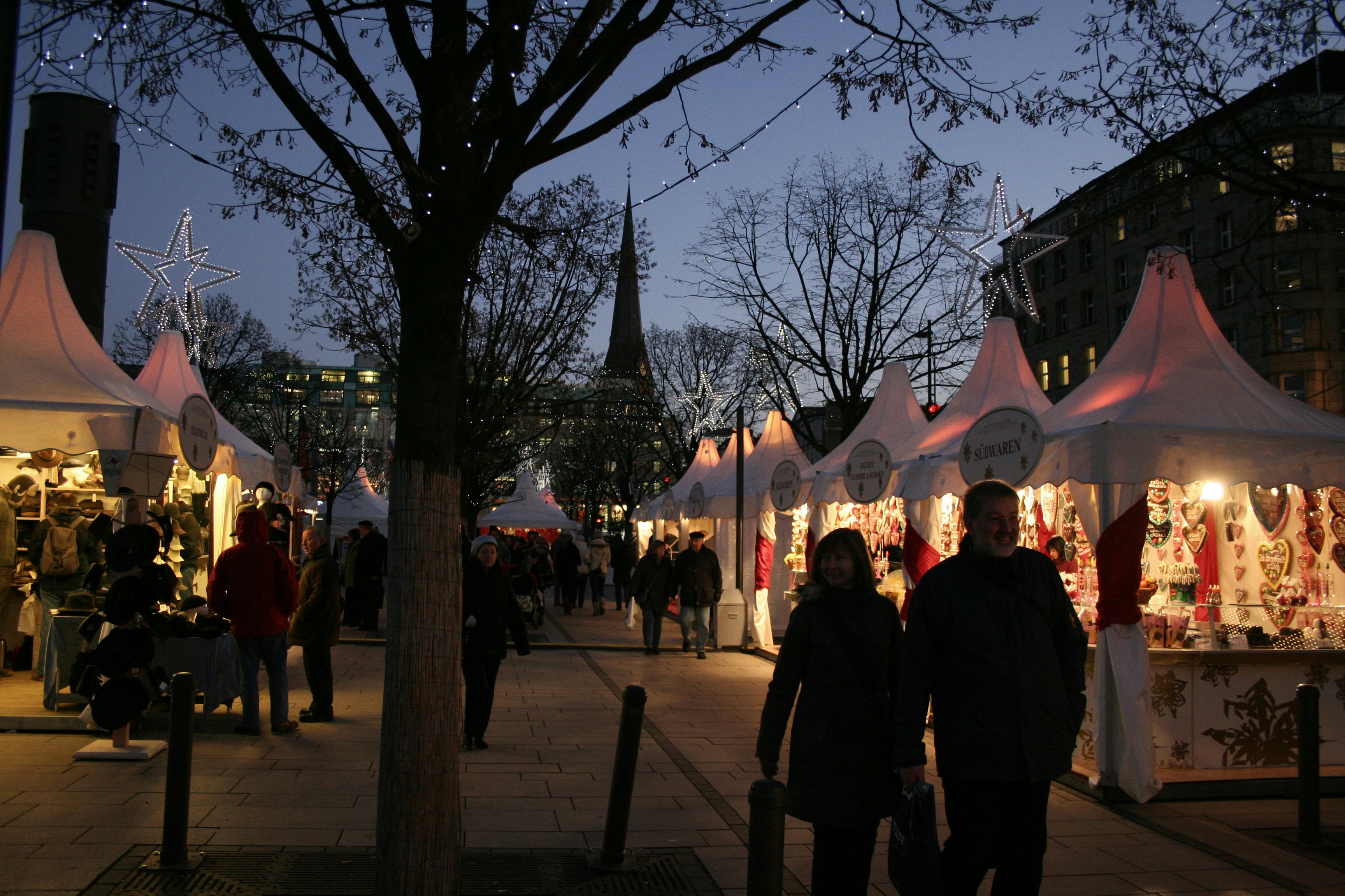 A group of people walking down a street next to tents, Weihnachtsmarkt, Jungfernstieg, Hamburg