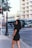 A woman in a short black dress standing on a sidewalk