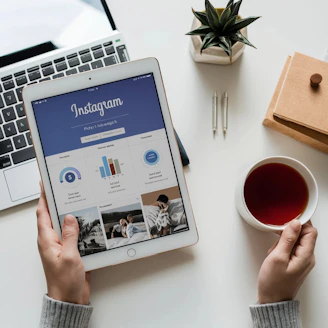 A person holding a tablet next to a cup of tea