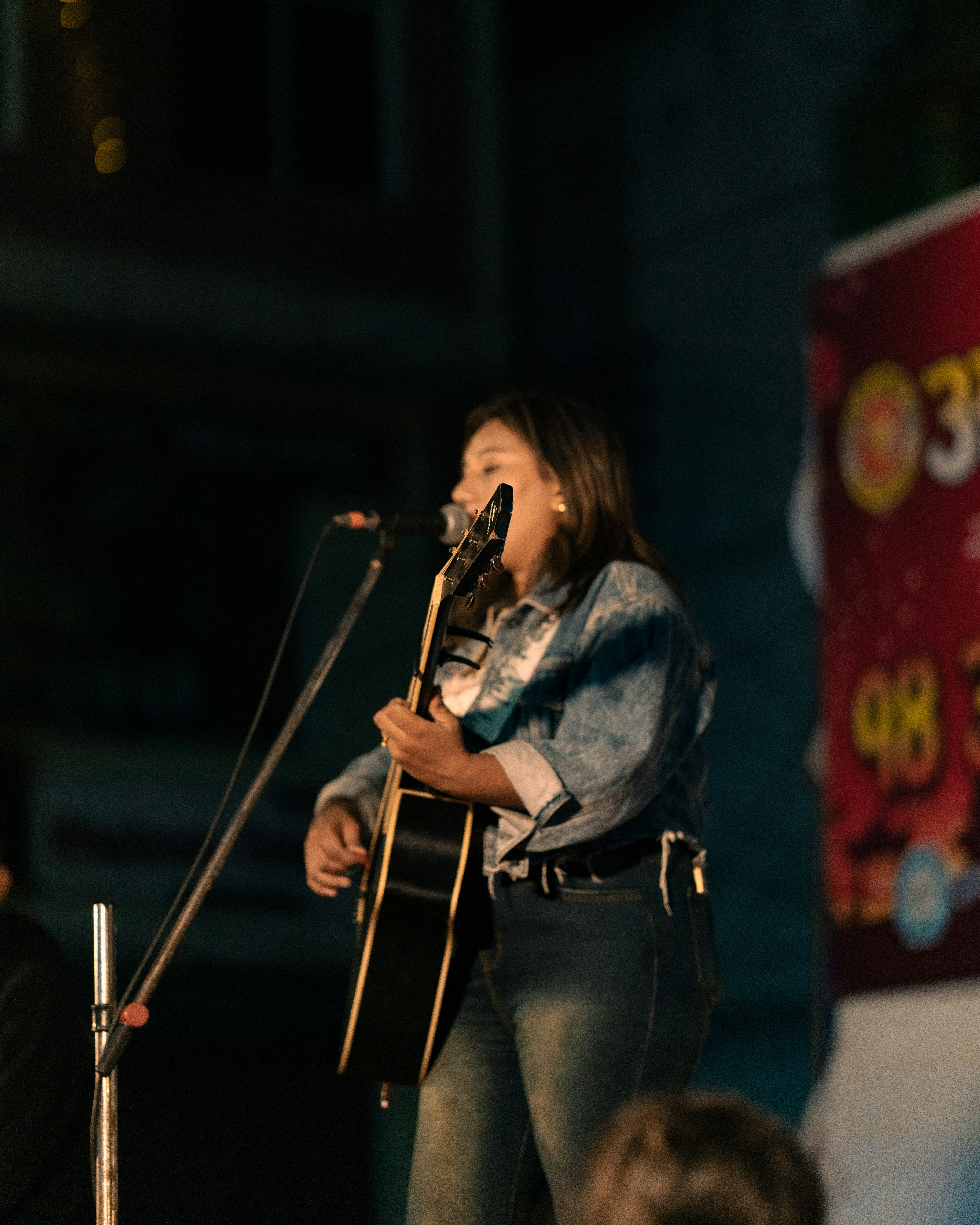 A woman singing into a microphone while holding a guitar