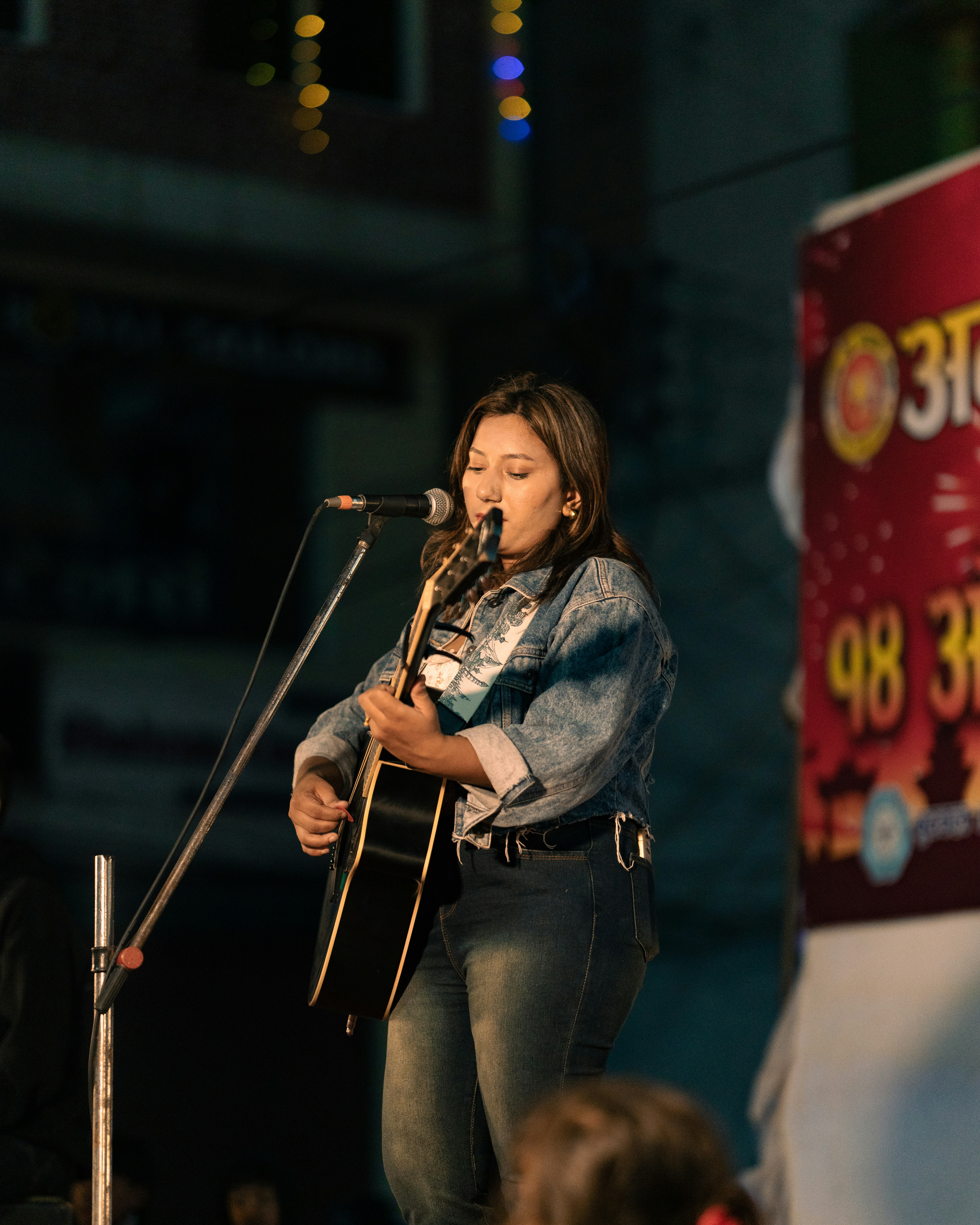 A woman standing in front of a microphone while holding a guitar