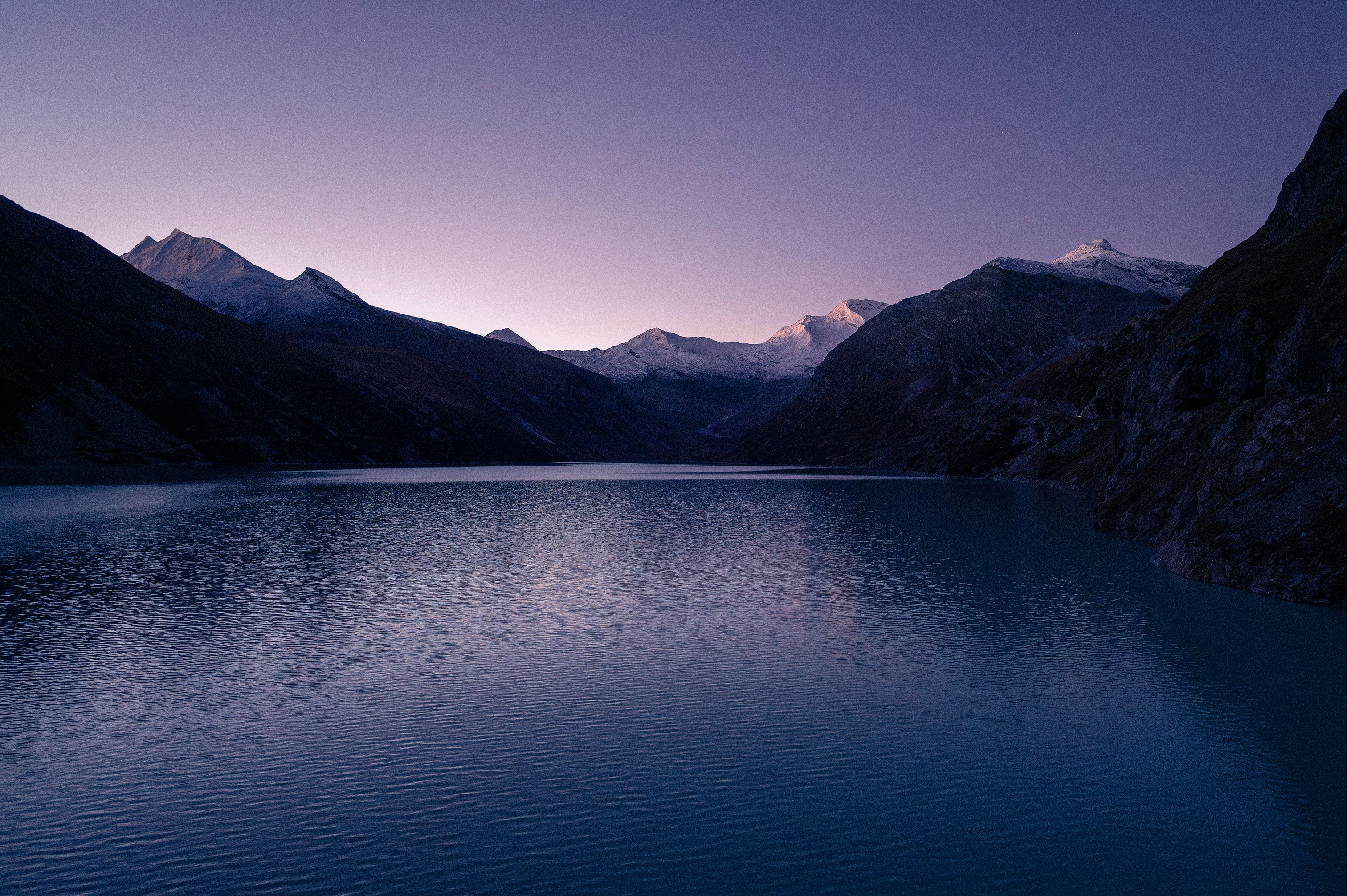 A body of water surrounded by mountains under a purple sky