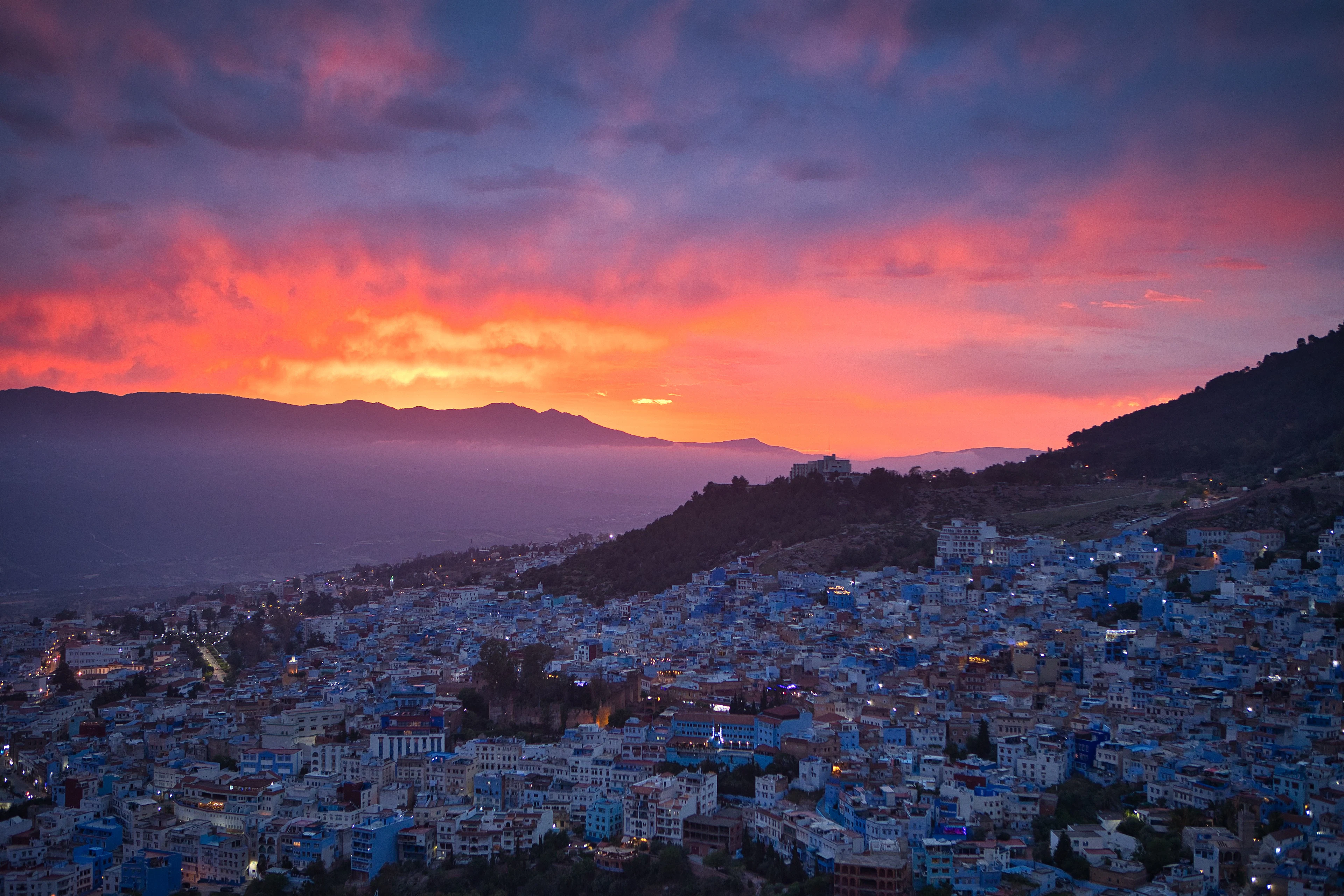 The town of Chefchaouen under a pink and orange sunset sky, with a mountain rising behind it