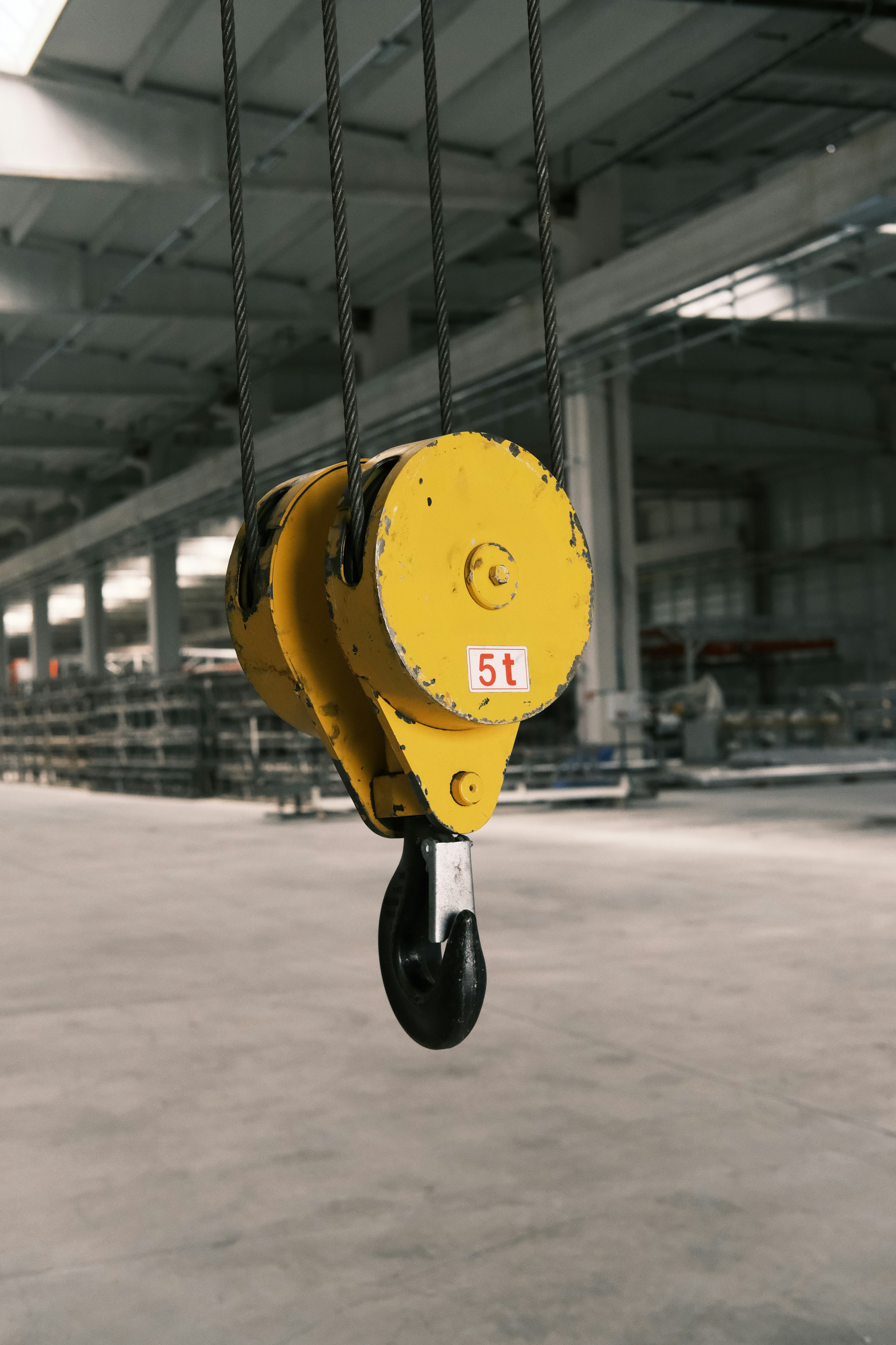 A yellow crane hanging from a chain in a warehouse