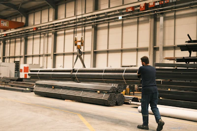 A man standing in a warehouse next to a pile of steel pipes