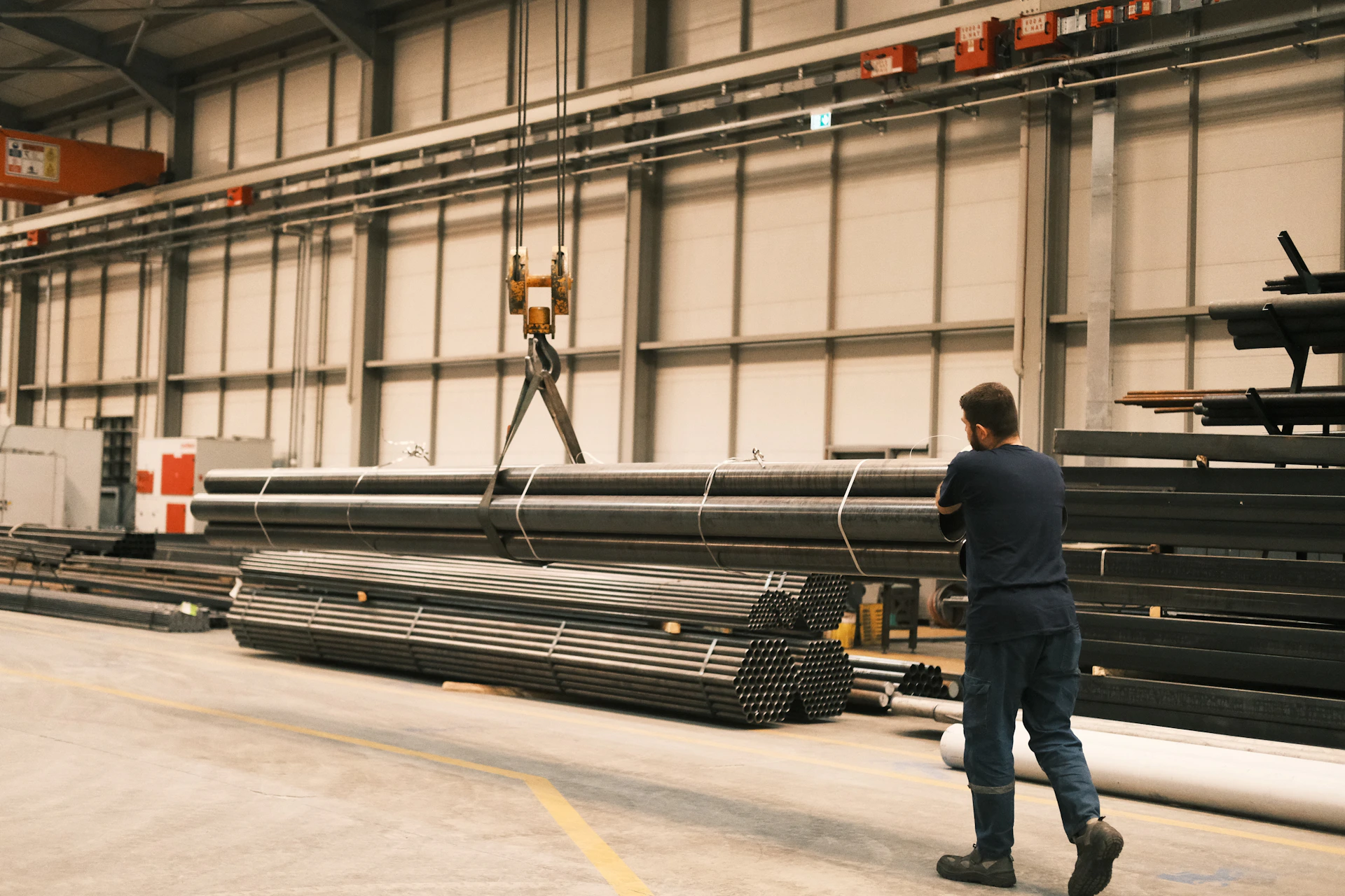 A man standing in a warehouse next to a pile of steel pipes