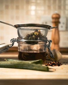 A glass jar filled with liquid next to a metal strainer