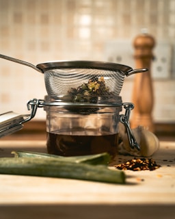 A glass jar filled with liquid next to a metal strainer