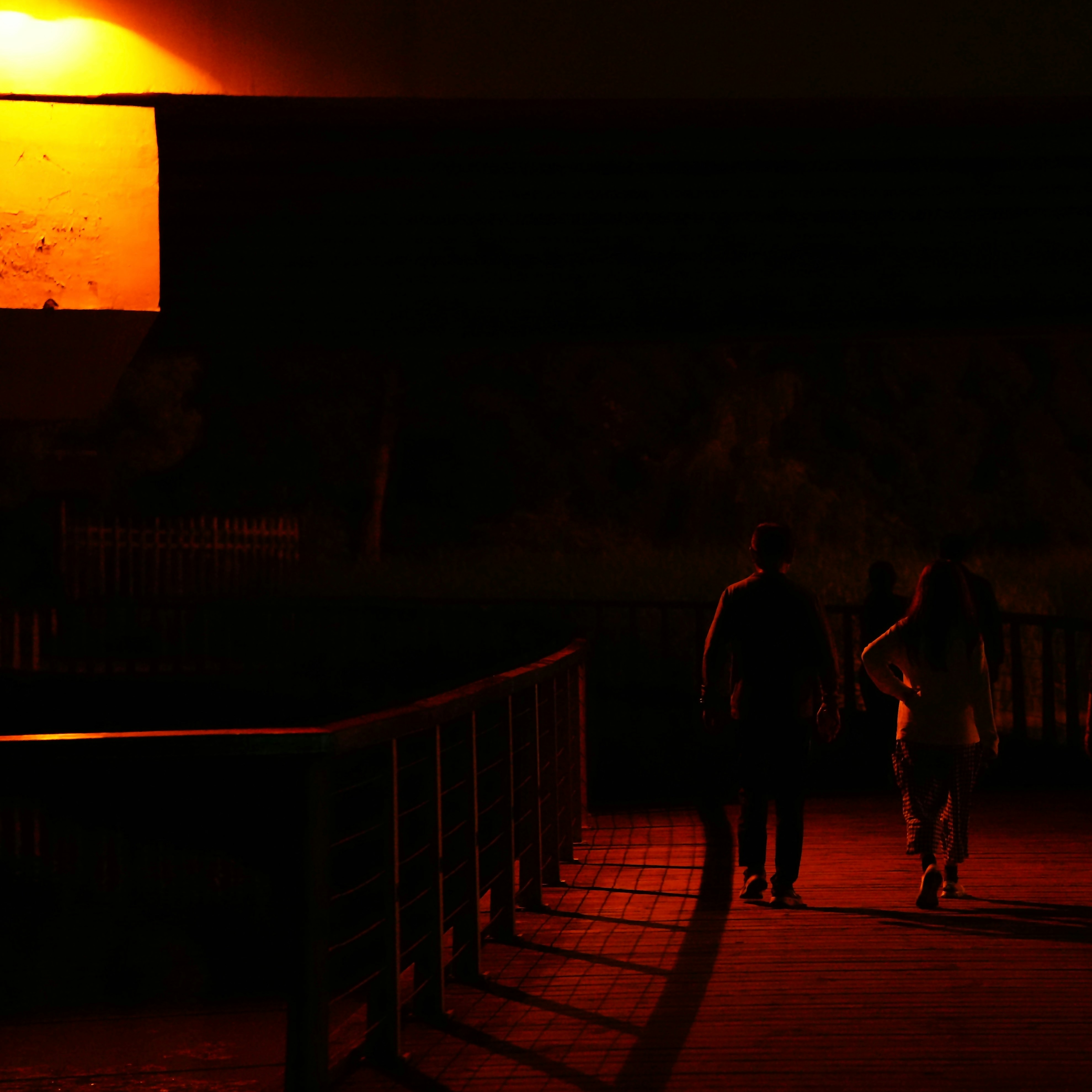A couple of people walking across a bridge at night
