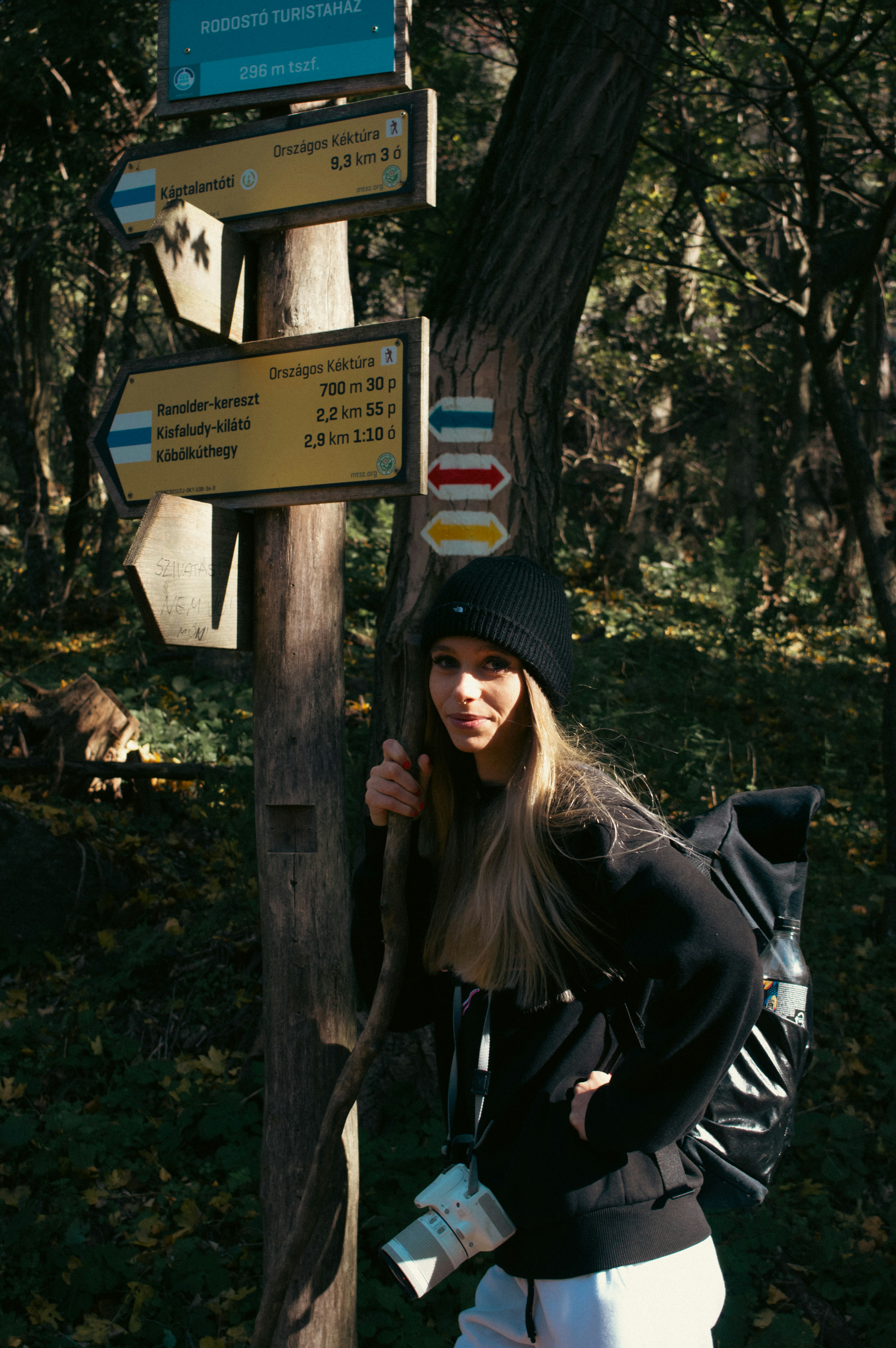 A woman standing next to a wooden sign post