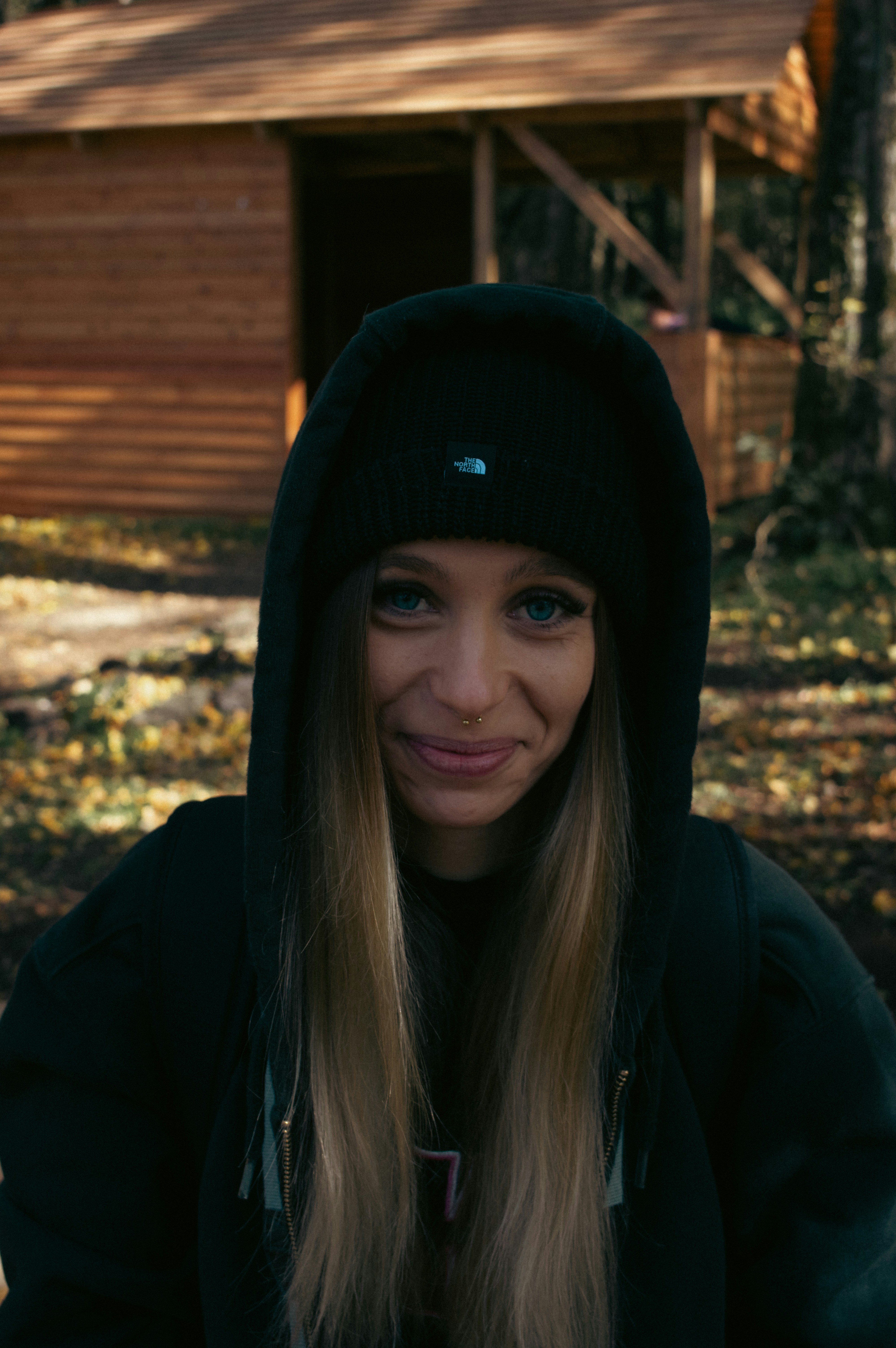 A woman in a black hoodie standing in front of a cabin