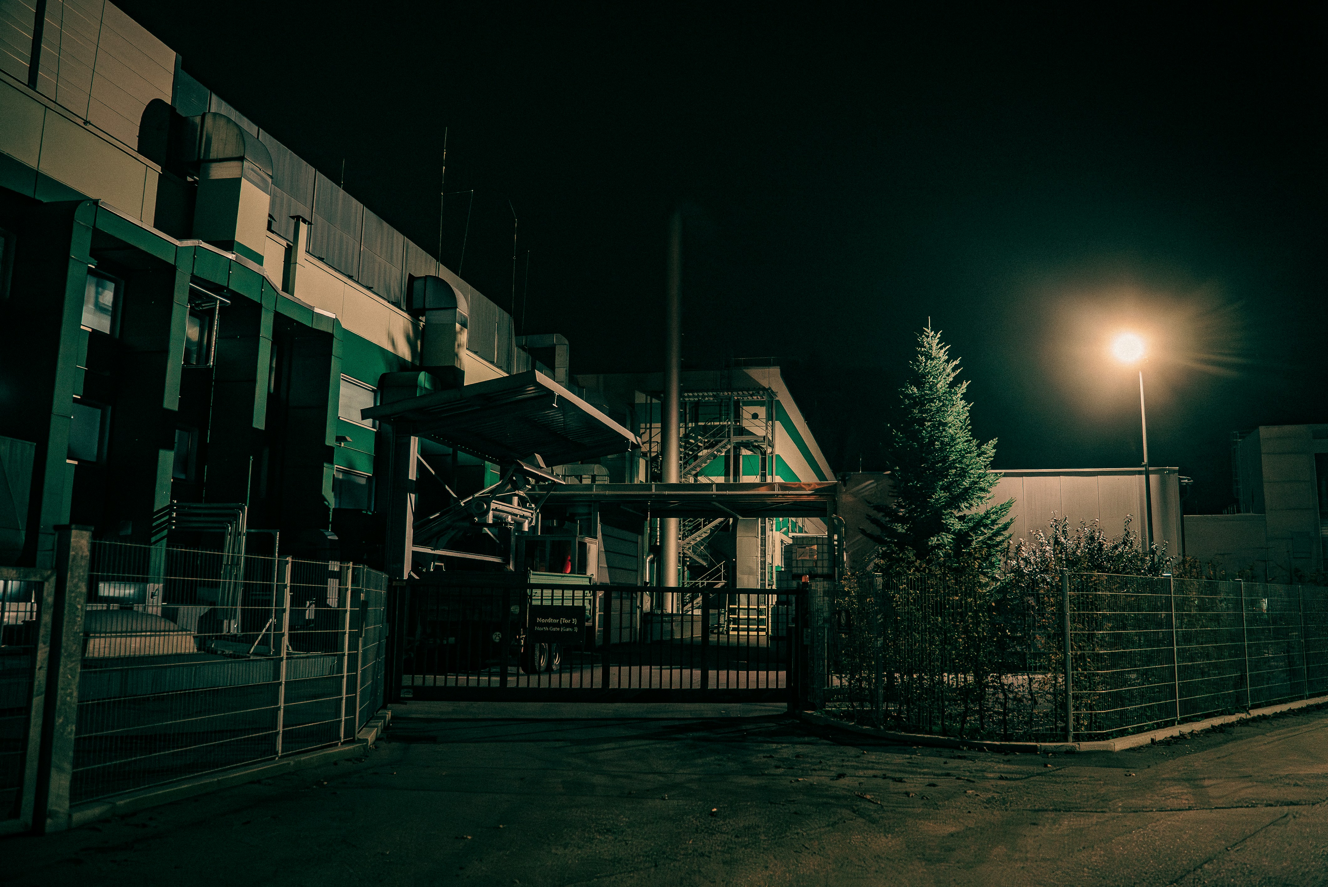 A street at night with a fence and a building in the background